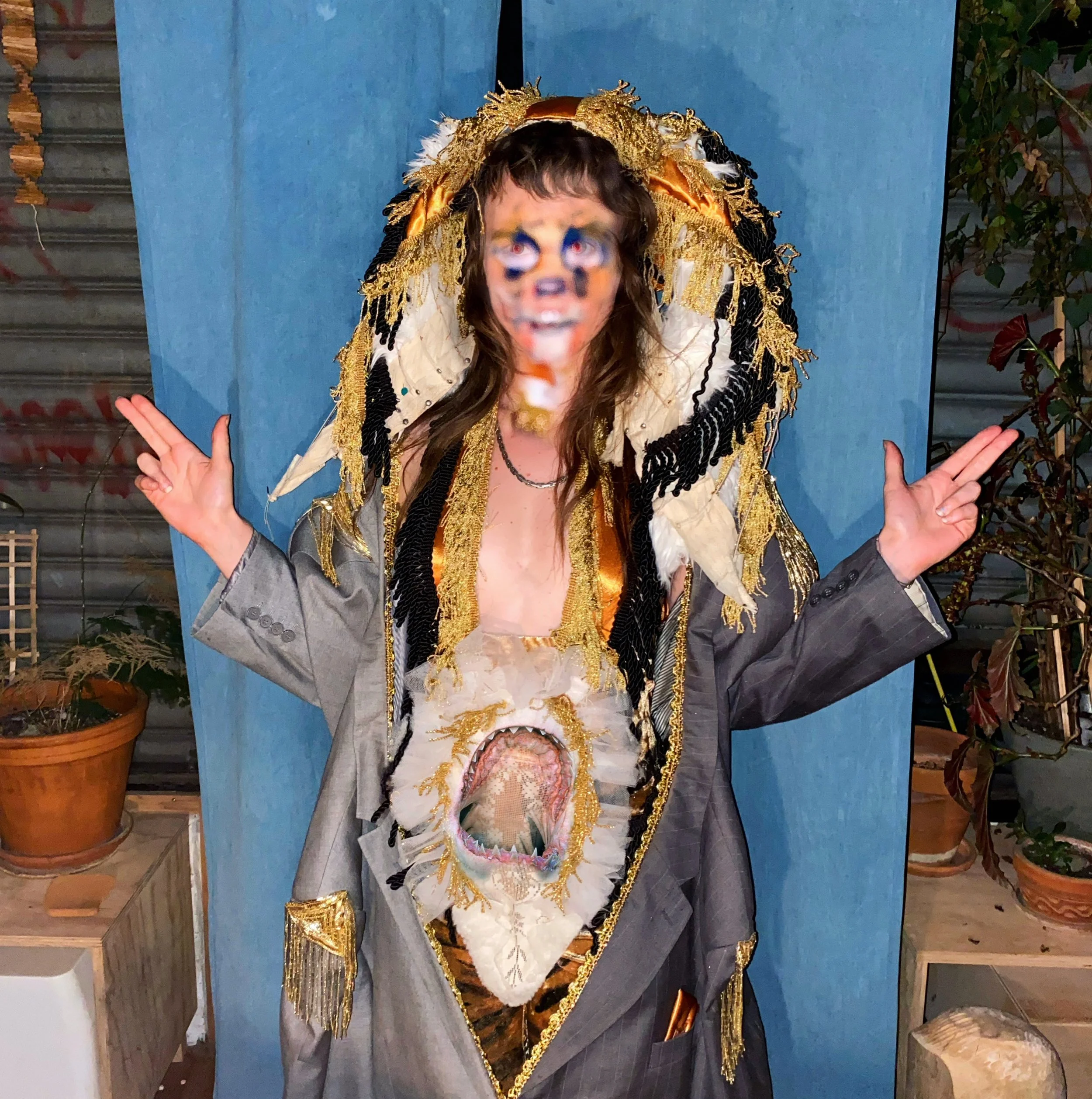 Lucia weawring one of her costumes, a tiger costume, with an edited image of a tiger mouth eating a lace opening att he center of their belly. Their chest shows but their face is painted with airbrush tiger stripes.