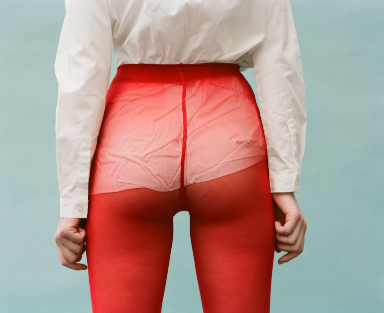 Person wearing red sheer tights with a white shirt, standing with their back facing the camera.