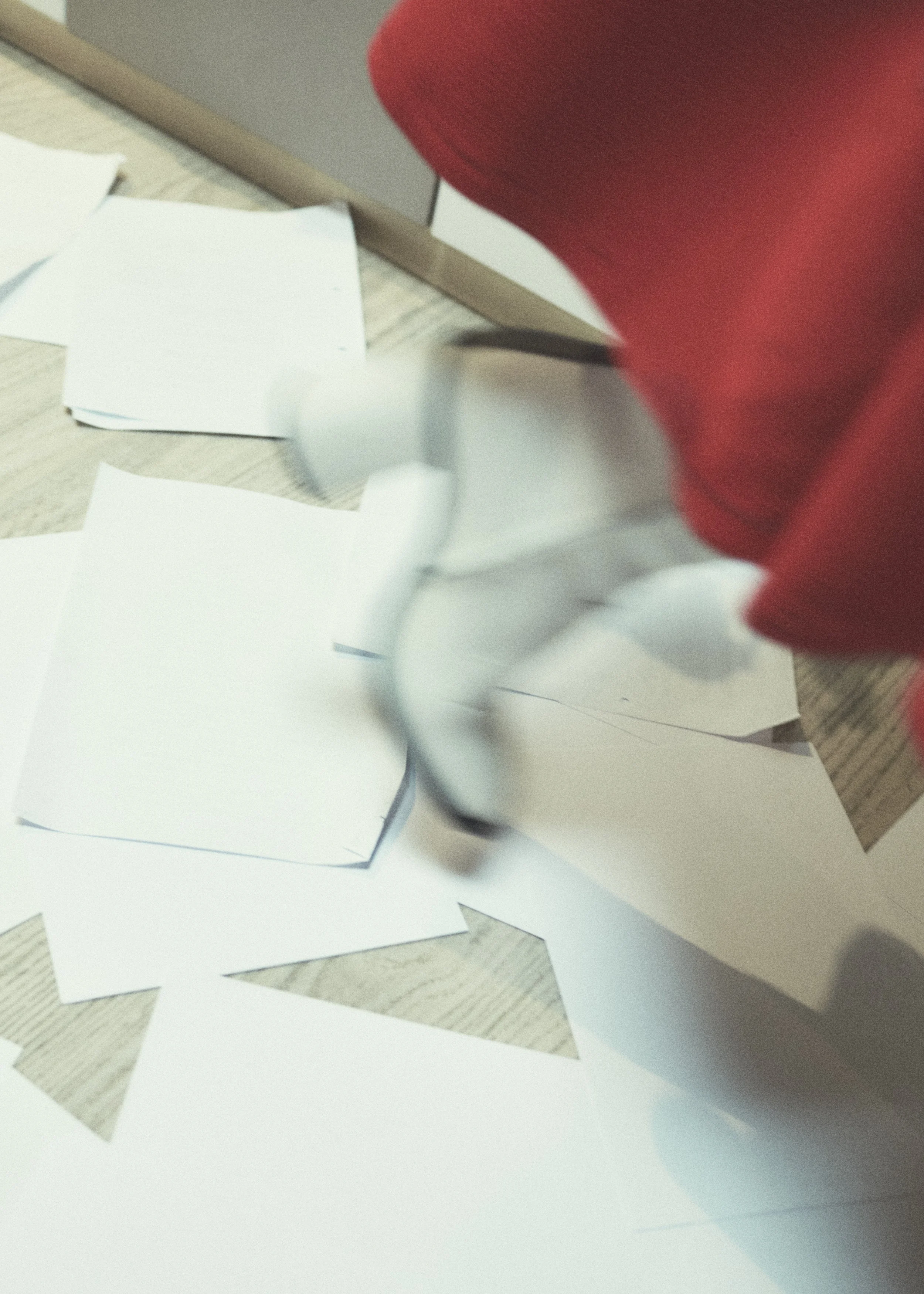 Person tearing a sheet of white paper with cut-out shapes on a wooden table.