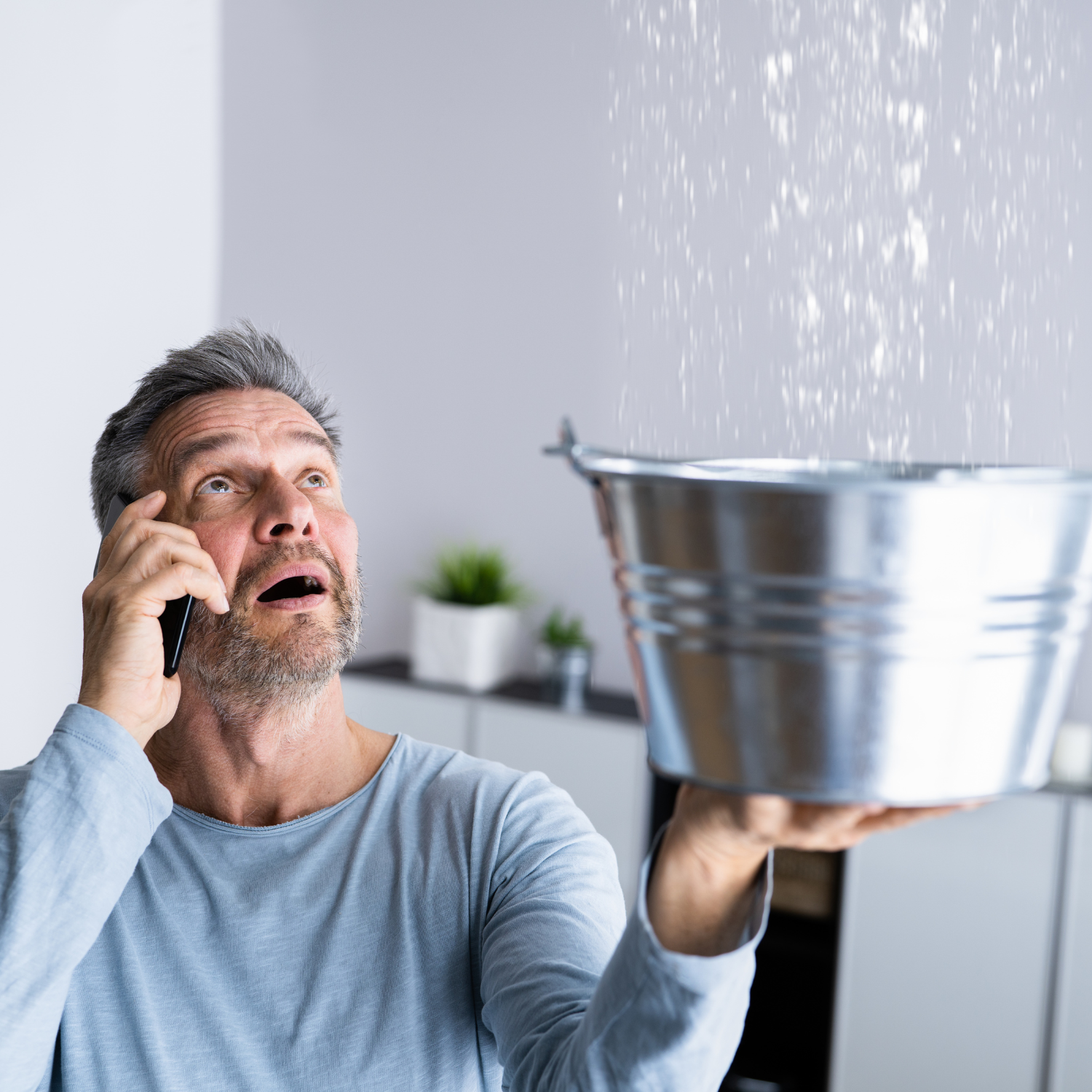 Homeowner catching a ceiling water leak with a bucket while calling for water damage repair