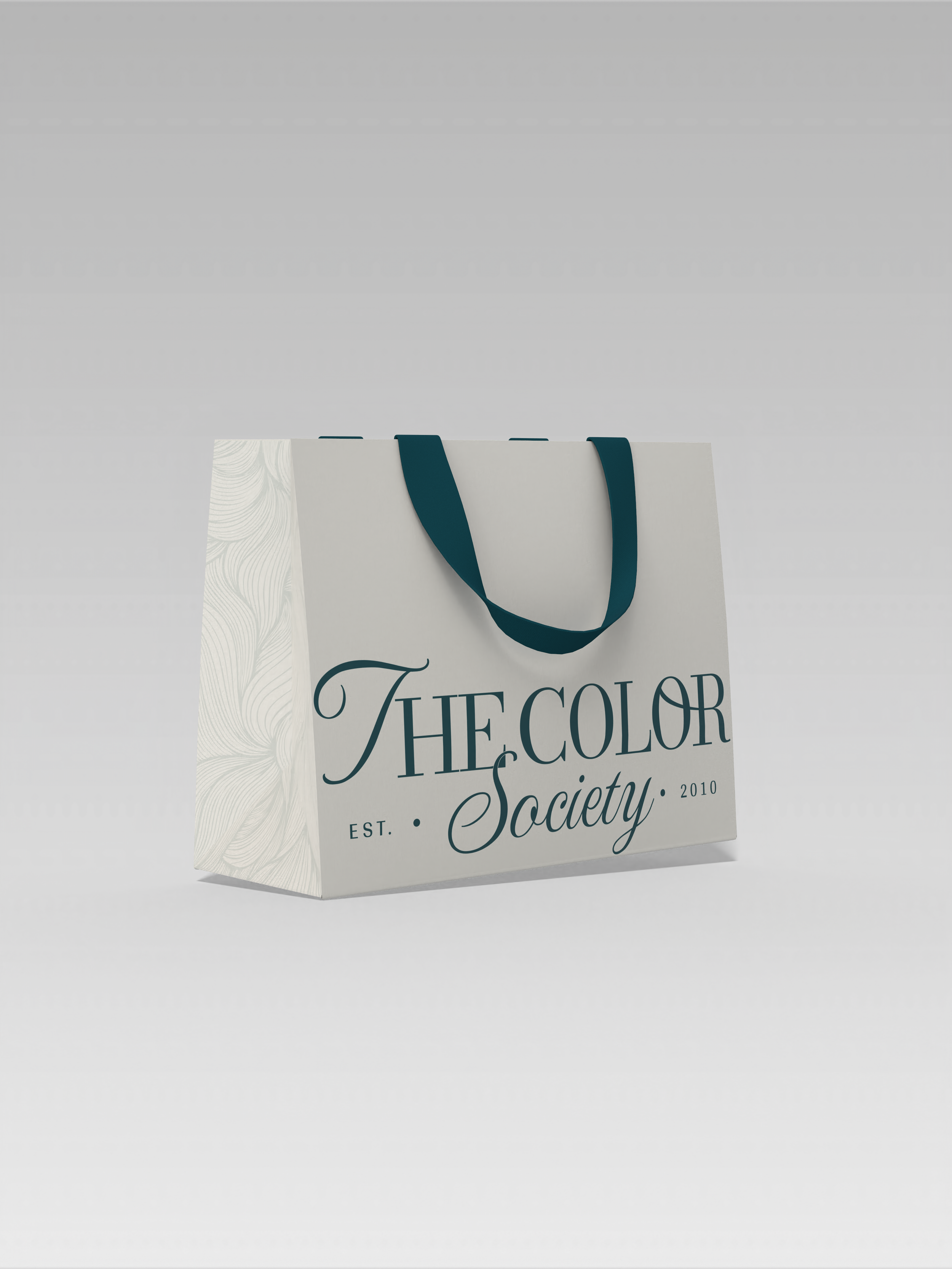 Una bolsa de papel blanca con asas azules, que lleva la leyenda 'The Color Society, Est. 2010' en letras elegantes.