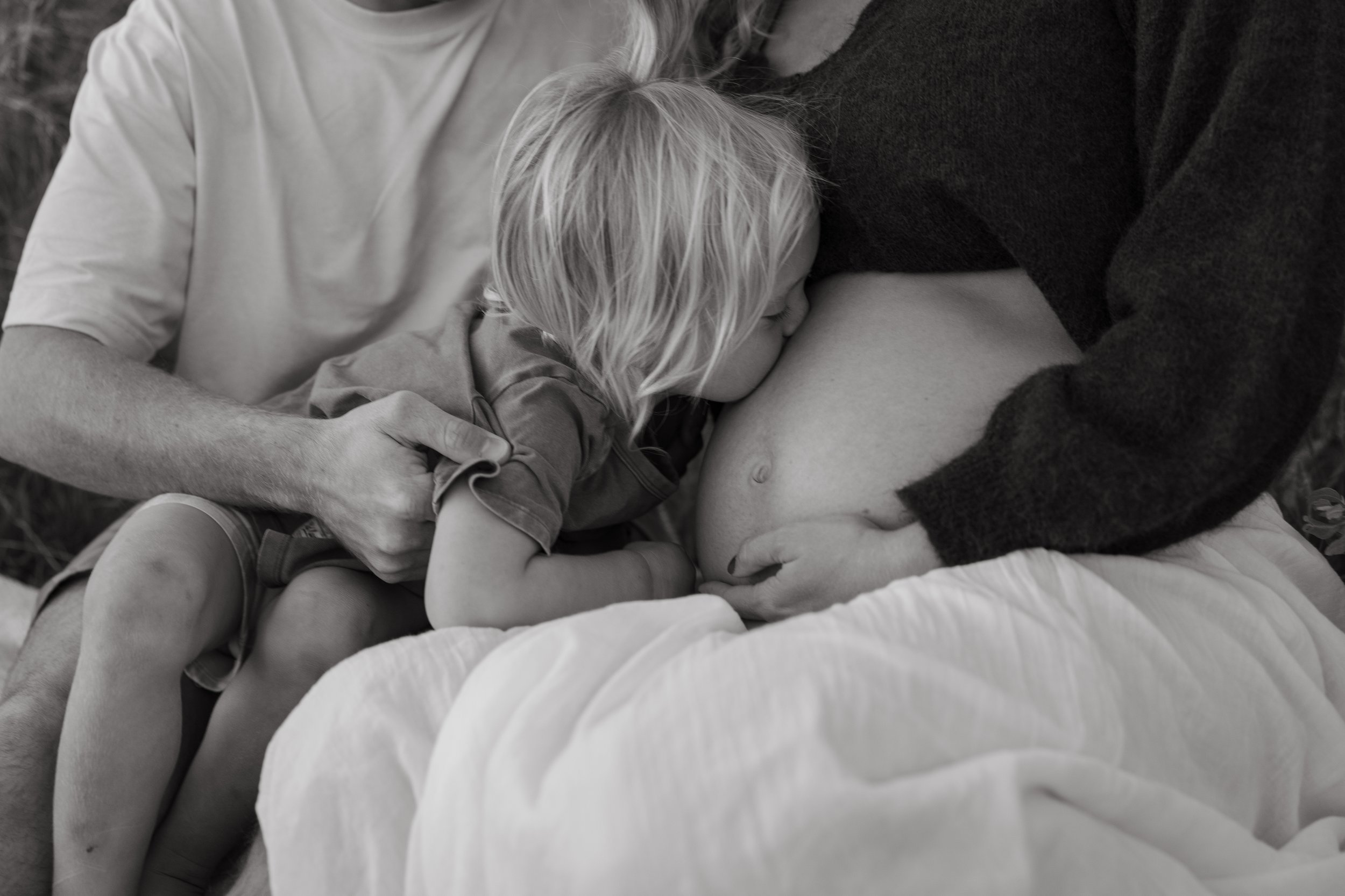 A person with light hair lying on their side with a child resting on their chest on a bed.