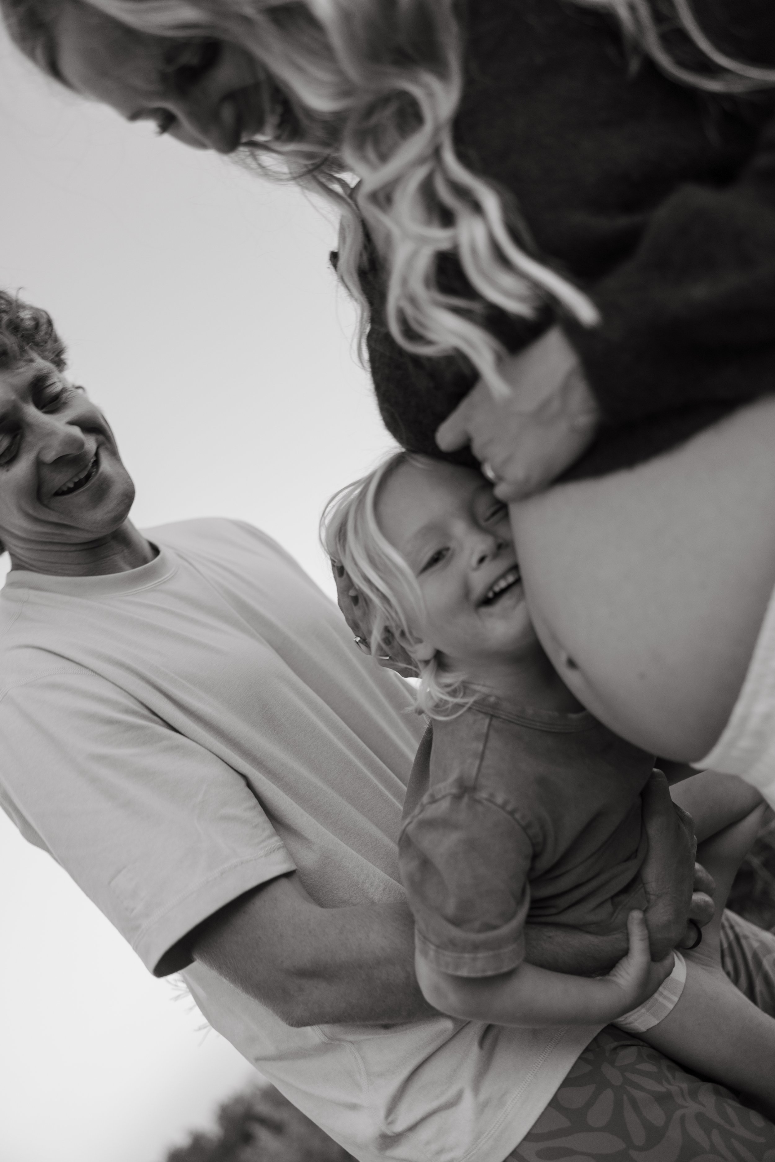 A man and two children are smiling and laughing, with the man holding the children in his arms. The image is black and white.