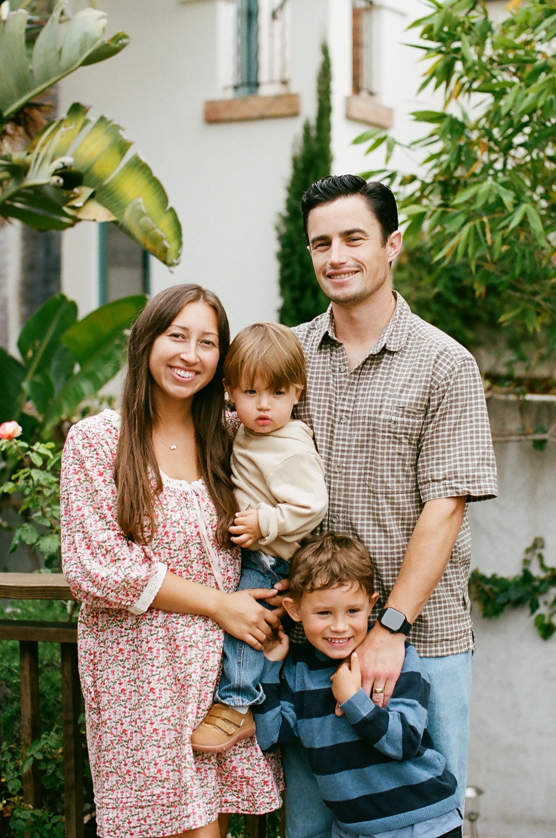 A happy family of six posing outdoors in a garden, smiling at the camera.