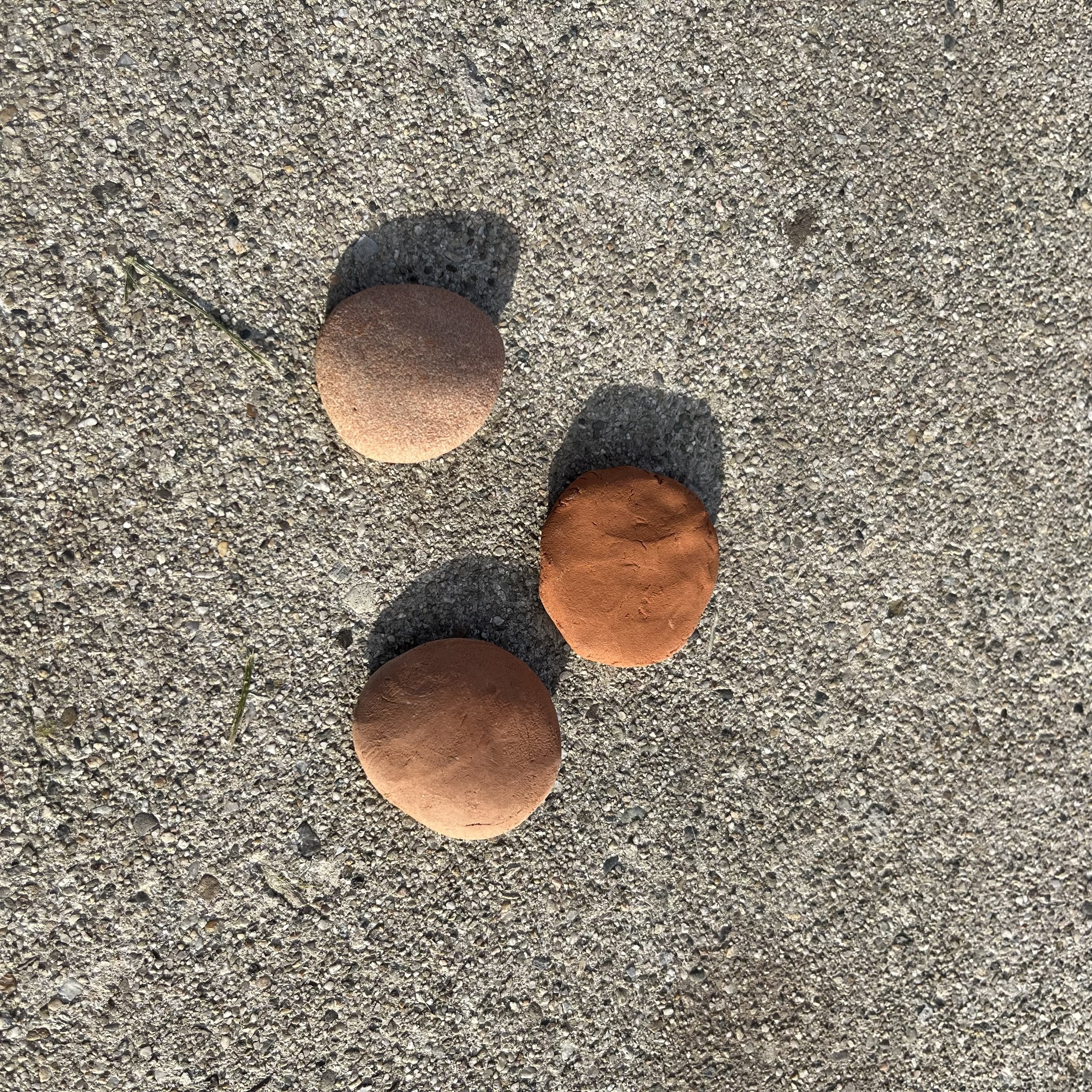 Close-up of several small, colorful clay stones on a textured sandy surface, with shadows cast by the stones.