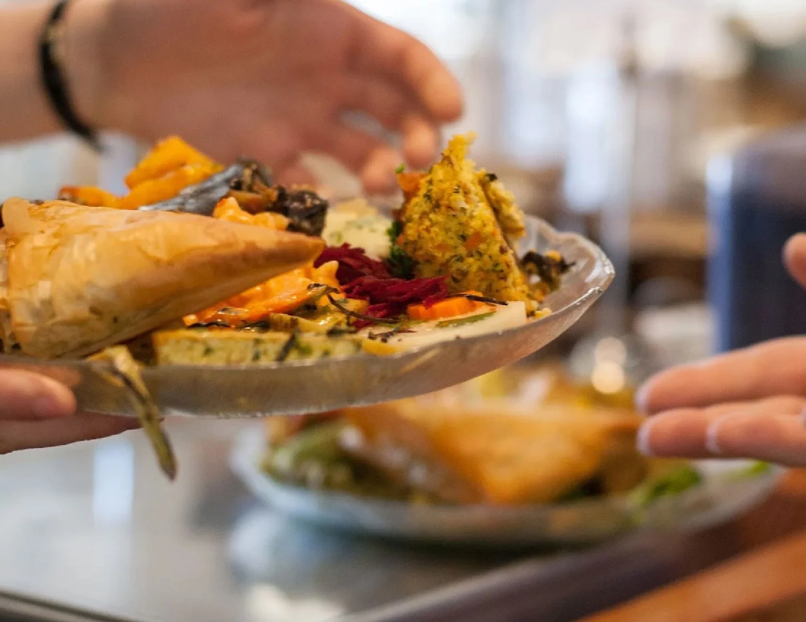 A person serving a plate of assorted pastry food, including rice, vegetables, and fritters, onto a dining table.