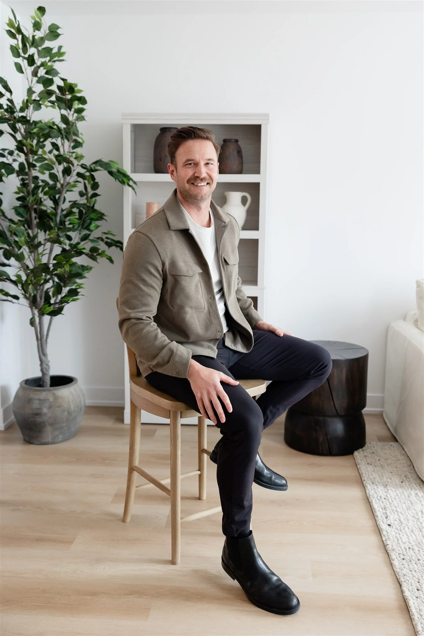 Smiling person in a gray blazer sitting indoors with a modern decor background.