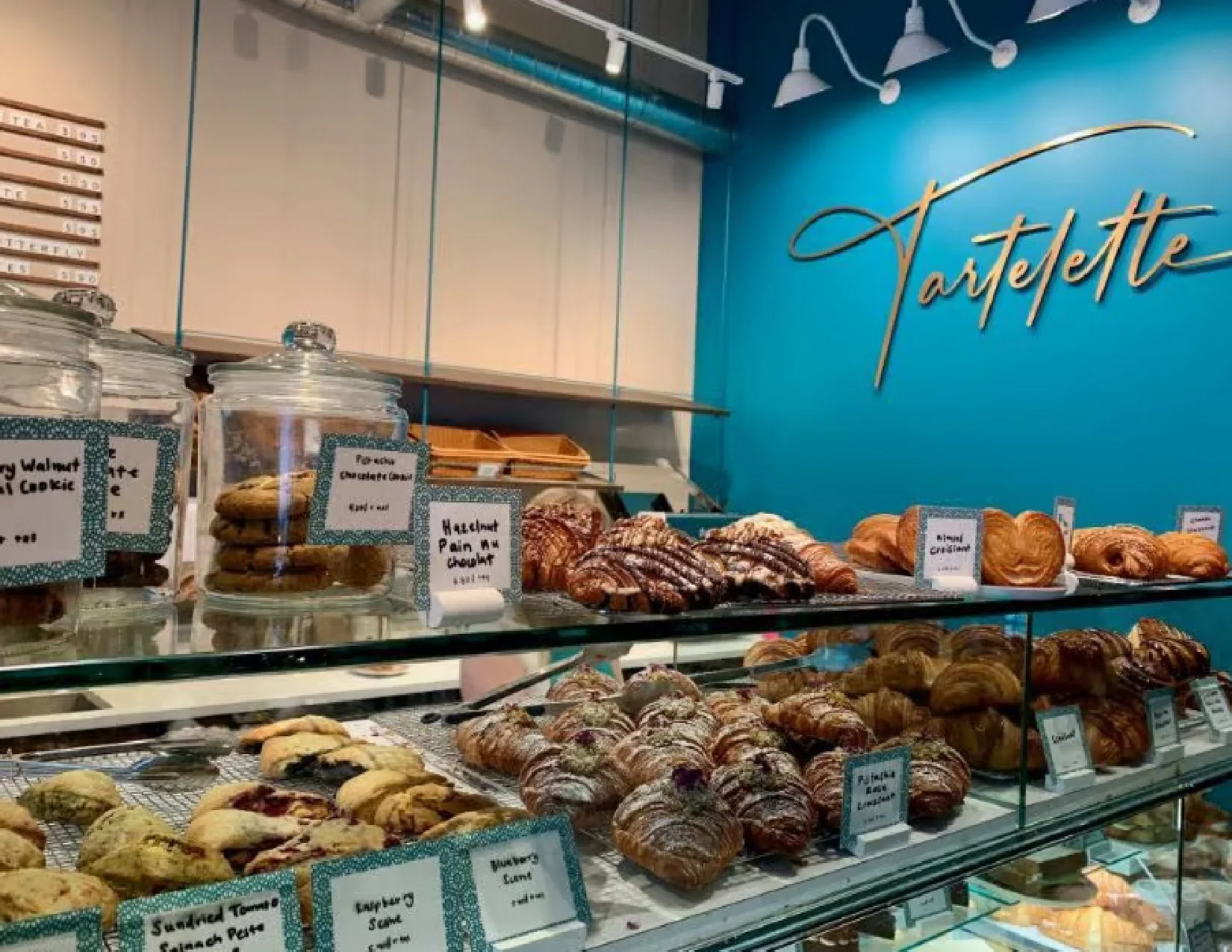 Display case with various baked goods including cookies, pastries, and croissants at a bakery with a bright blue wall and sign reading "Vartelet."