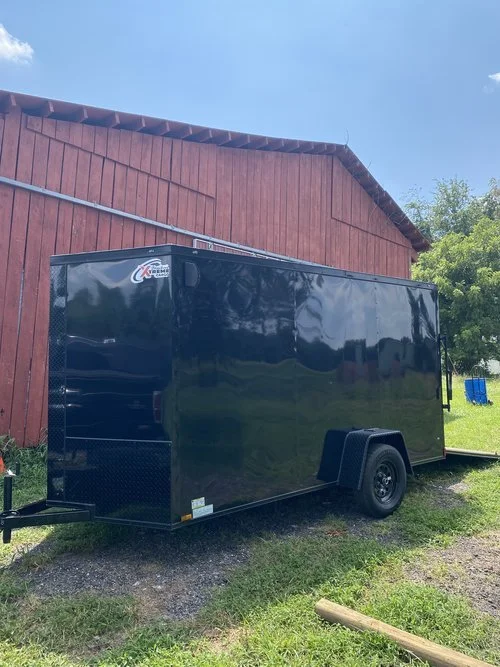 Black enclosed trailer parked on grass near red wooden building.