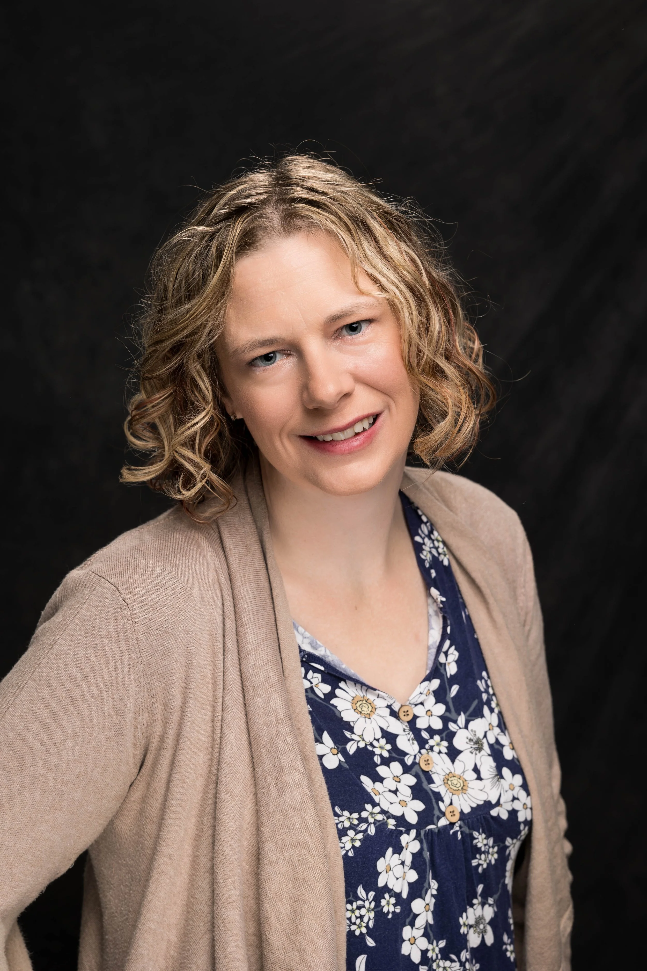 Therapist headshot. A woman with curly hair smiling at the camera.
