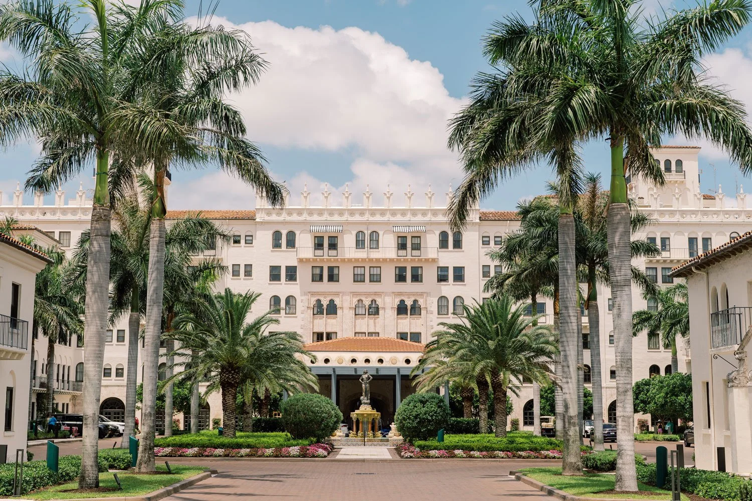 The Boca Raton Resort entrance, showcasing a majestic white building with palm trees and a fountain.