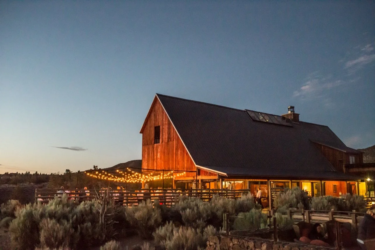 A rustic barn at Brasada Ranch with string lights and a deck overlooking a scenic landscape.