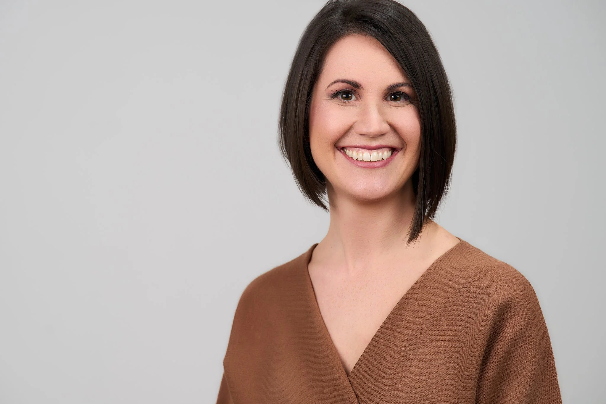 Headshot of Laura Winters with dark brown hair and a tan top, smiling