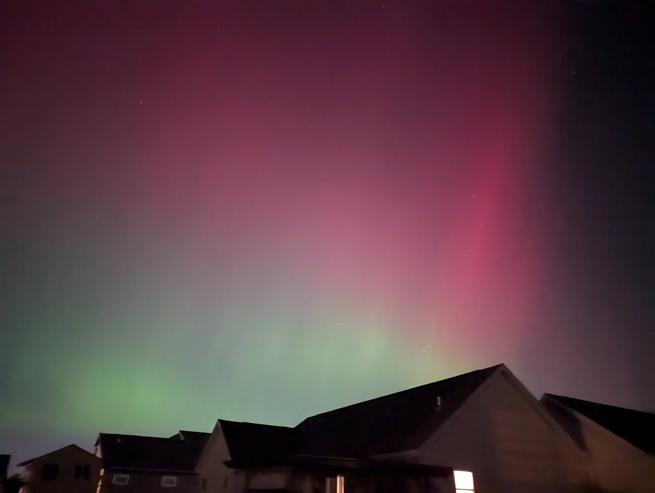 Northern lights displaying pink and green colors over a neighborhood with houses at night.