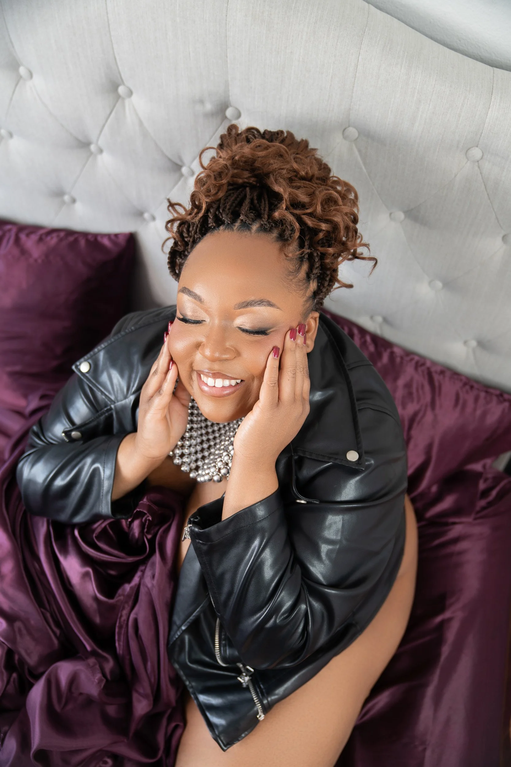 woman with dreadlocks in leather jacket on maroon satin sheets