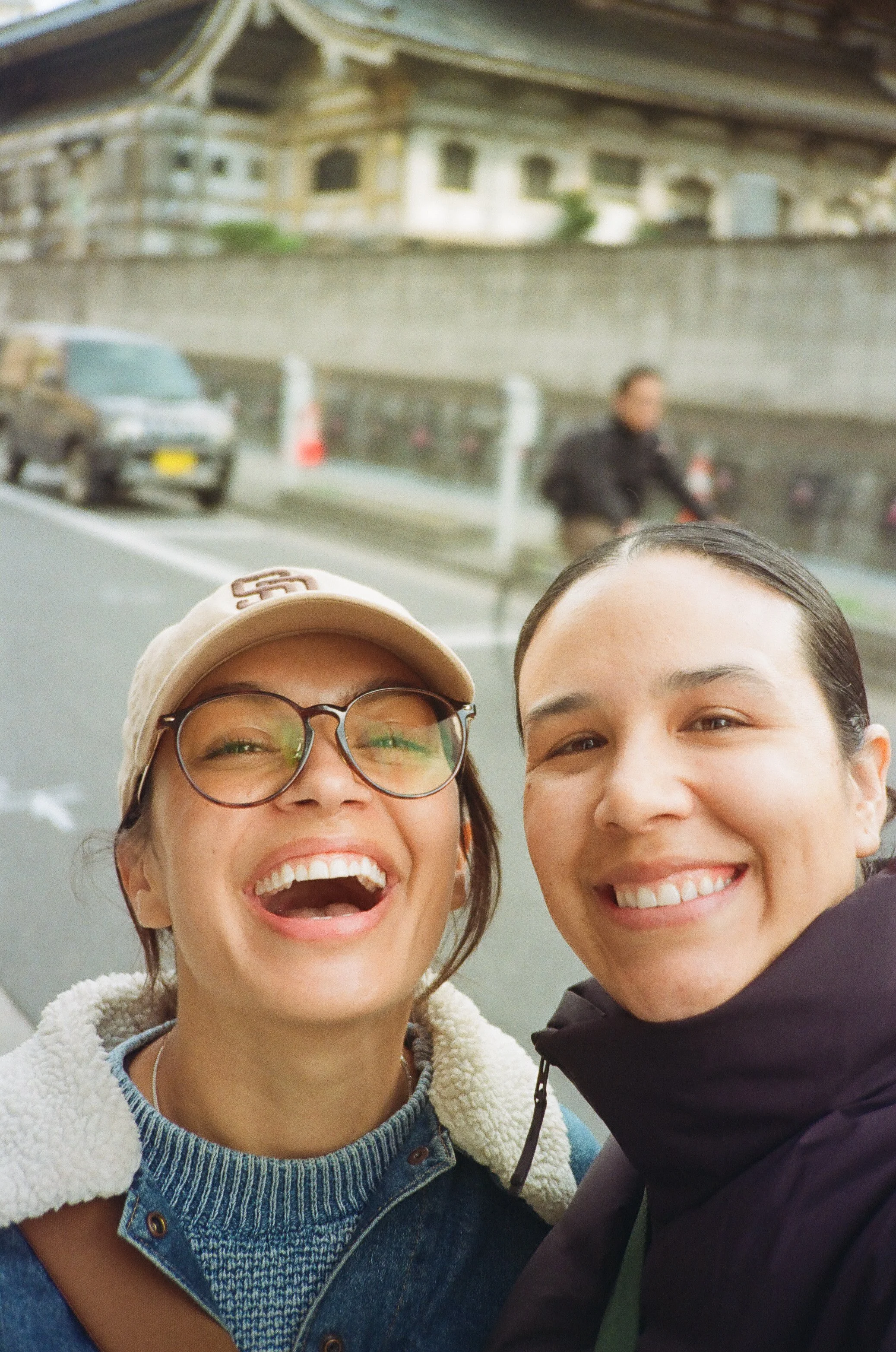 Two smiling women taking a selfie outdoors in an urban area.