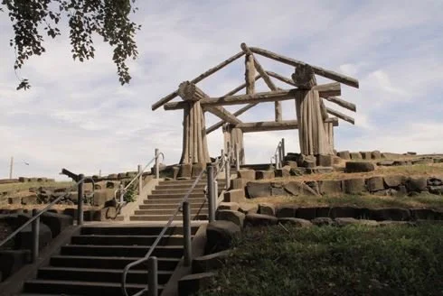 Wooden structure resembling a traditional Japanese torii gate on a hill with stairs leading up to it, under a cloudy sky.