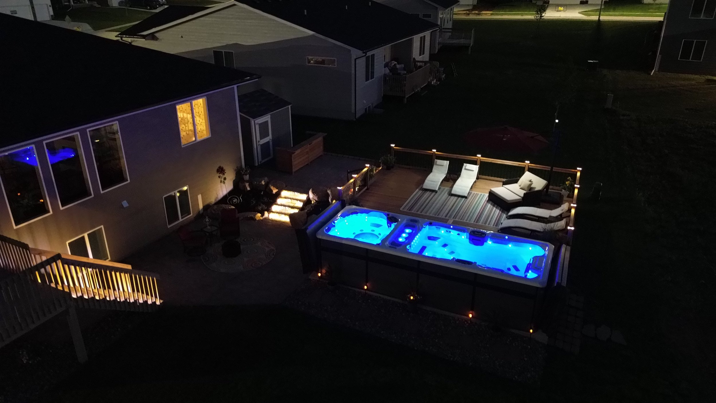 Nighttime aerial view of a backyard deck with a lit swim spa