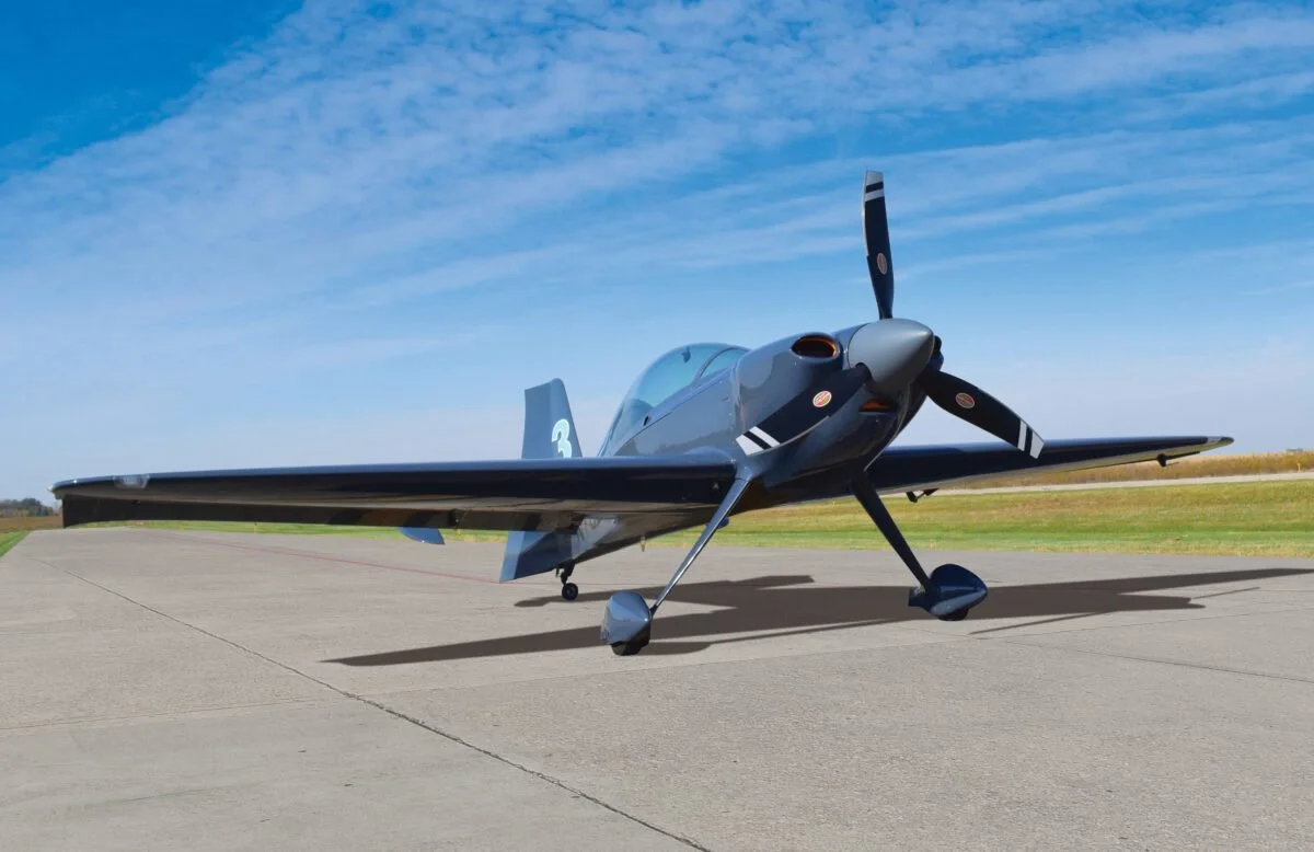 Aerial view of five planes flying over the Golden Gate Bridge, including a red aerobatic aircraft and four blue fighter jets leaving white smoke trails, over the ocean and coastline.