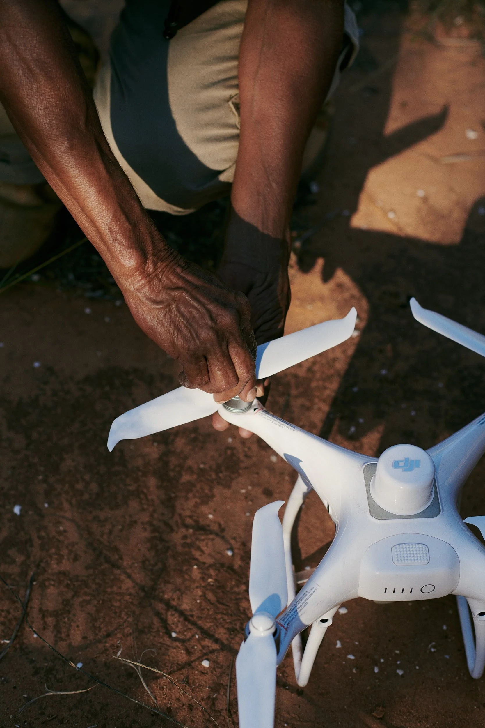 A person adjusting a DJI drone while it sits on red earth.