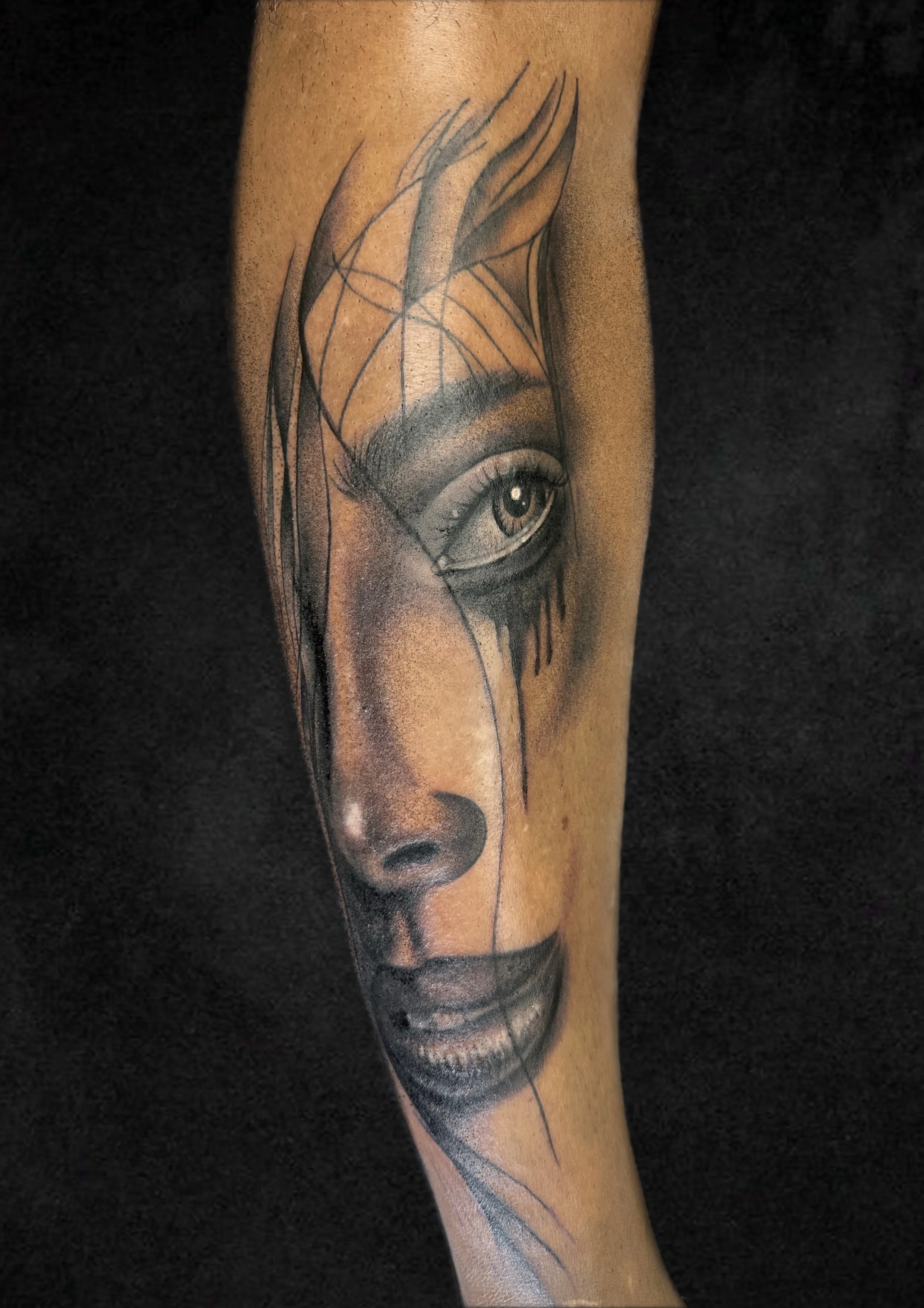Tattoo of a realistic woman's face with detailed shading, focusing on her eye, nose, and lips, with sketch-like lines extending from her forehead.