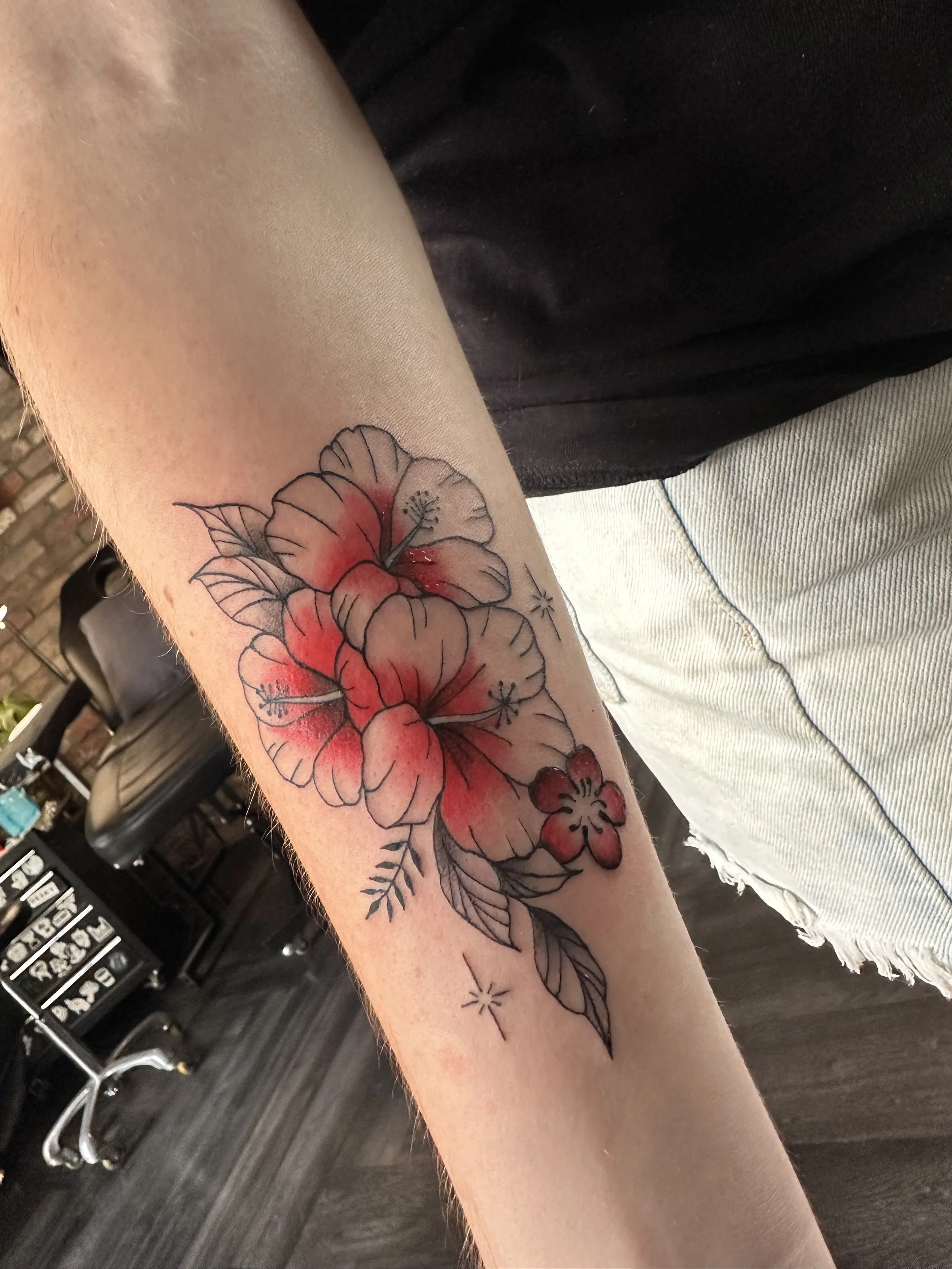 Tattoo of hibiscus flowers with red and black ink on the inner forearm.