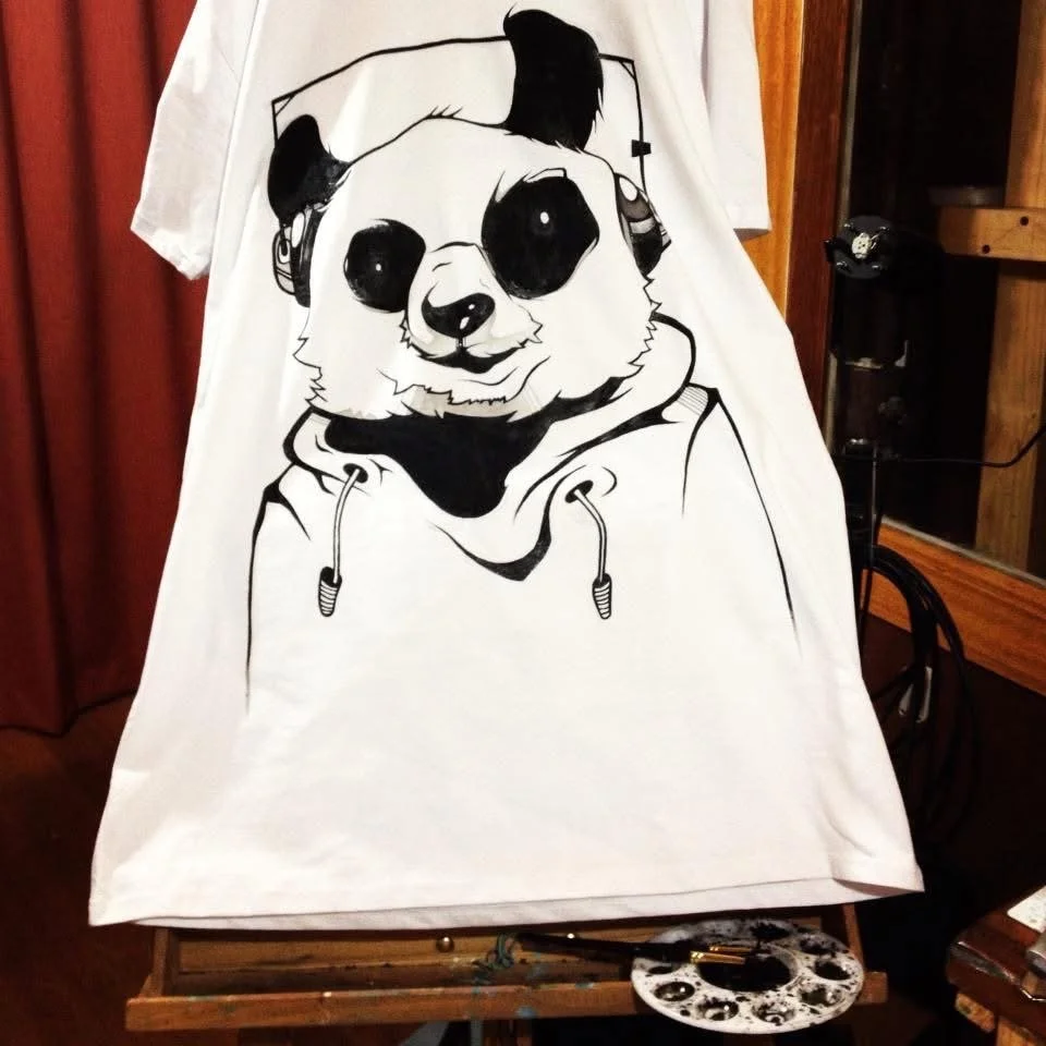 A white T-shirt with a black and white illustration of a panda bear wearing a hoodie.