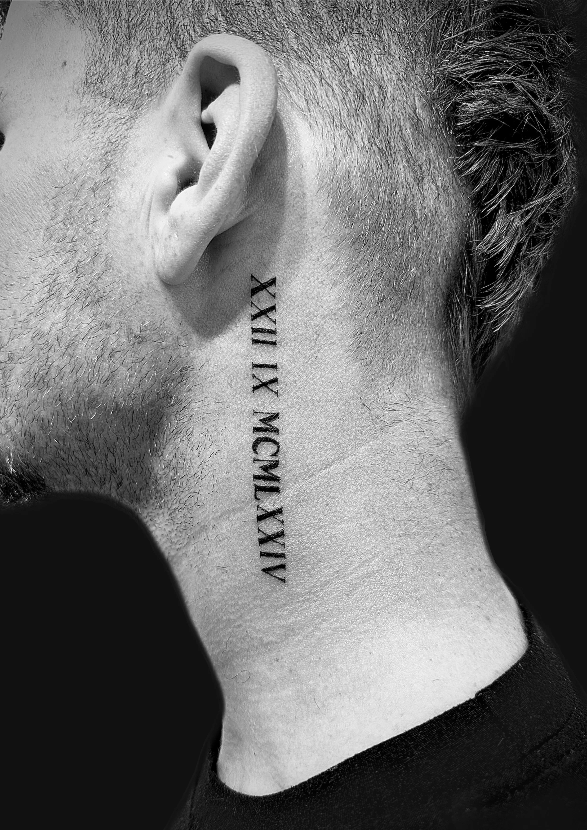 Close-up of a person's neck and ear, showcasing a vertical tattoo with Roman numerals.