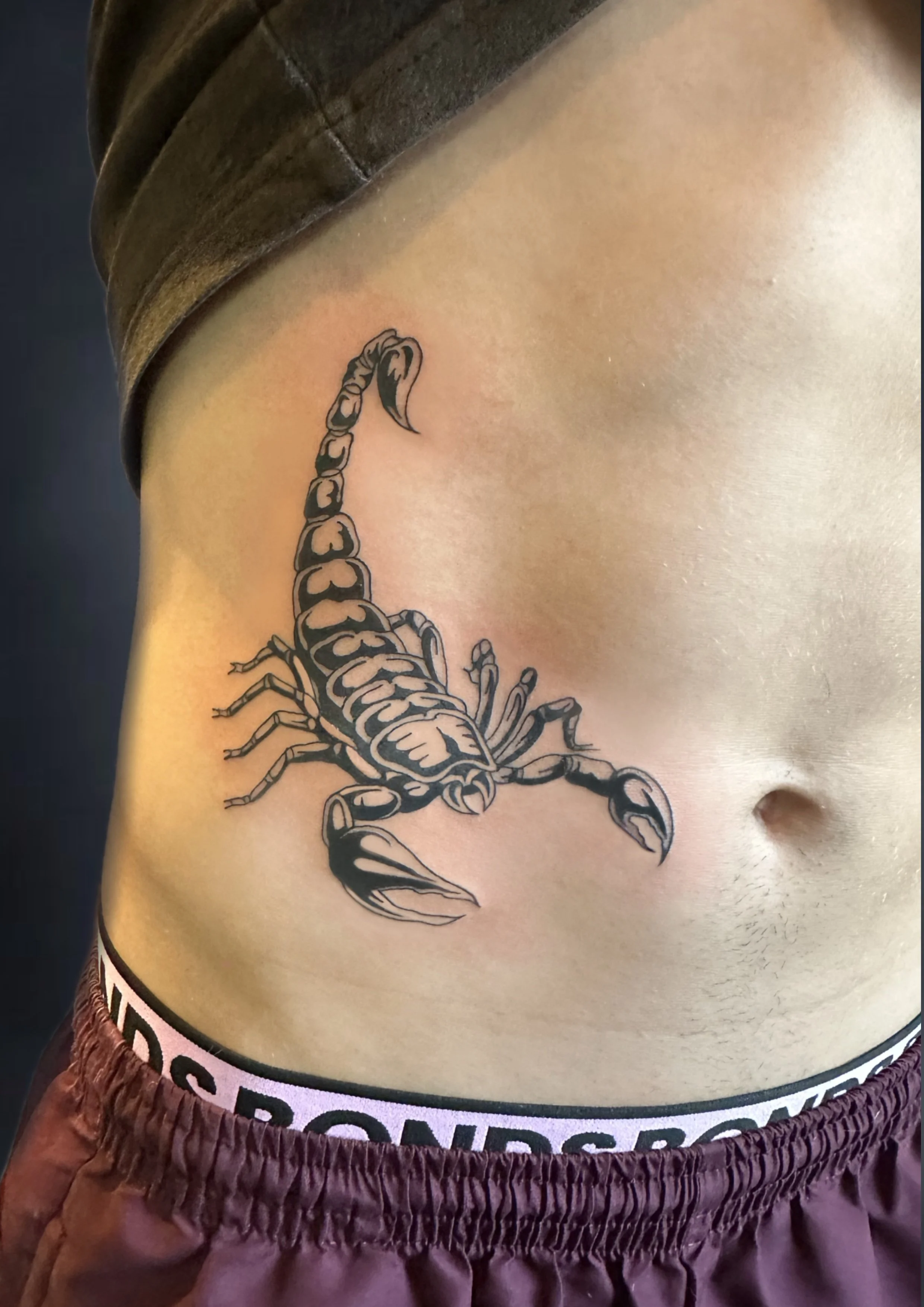Tattoo of a scorpion on a person's side abdomen, with the top part close to the person's chest.