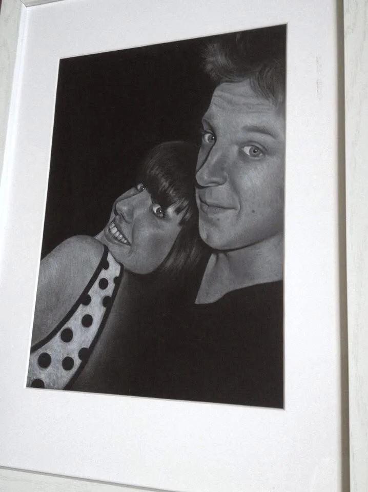 Black and white photo of a young woman and a young man taking a close-up selfie, both smiling.