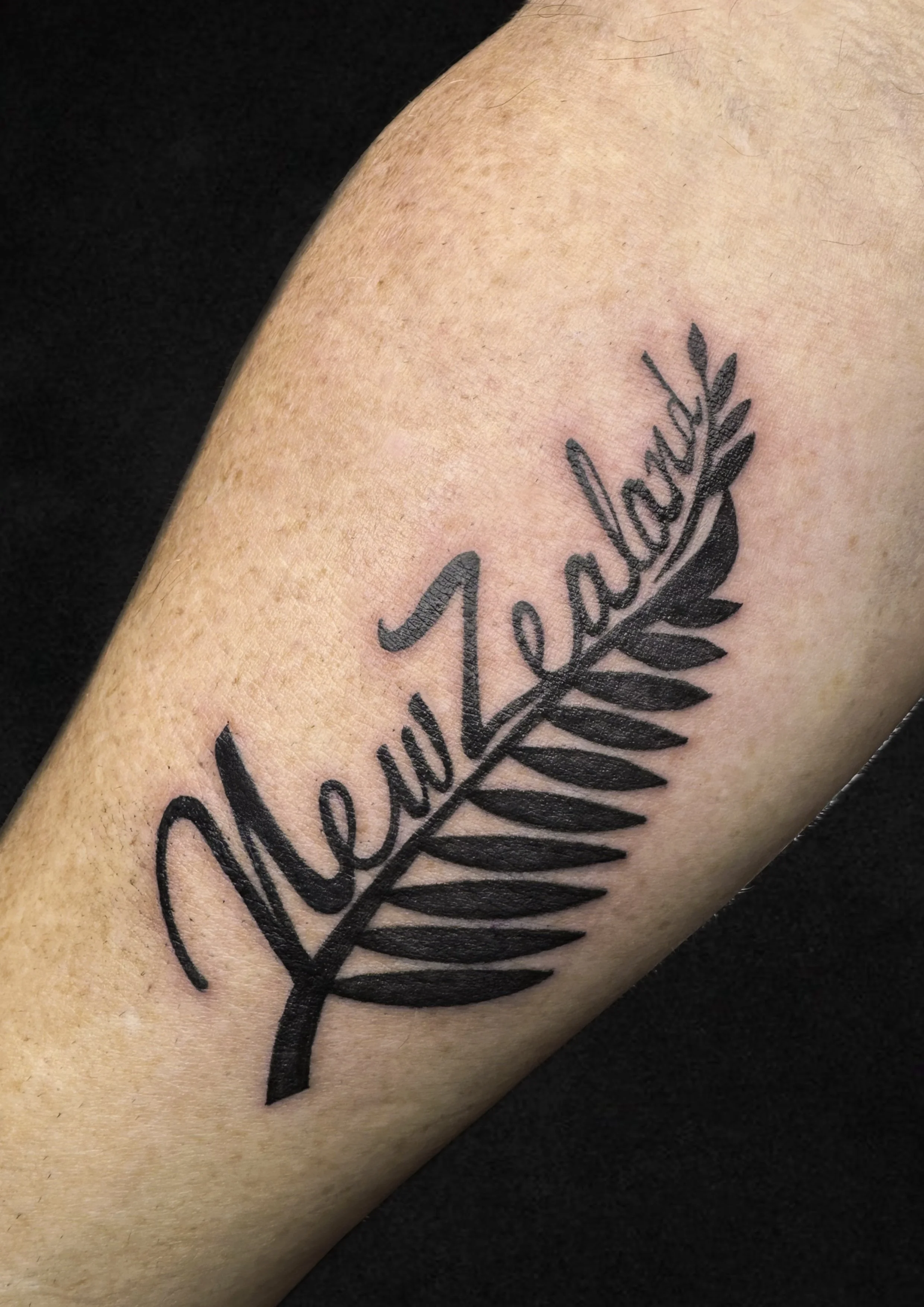 Tattoo of the word 'StaySea' in cursive script with a black fern leaf design below it on a person's arm.