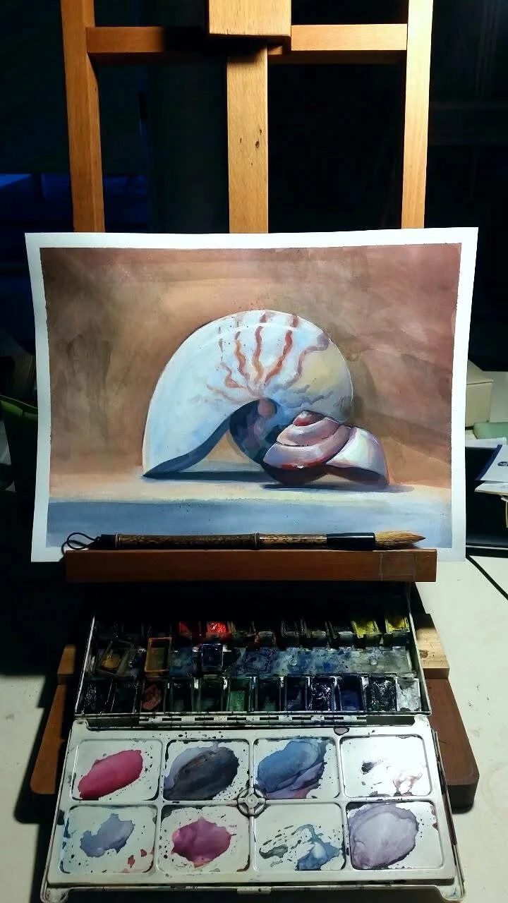 A watercolor painting of seashells on a table, with a watercolor palette and brush in front of it.