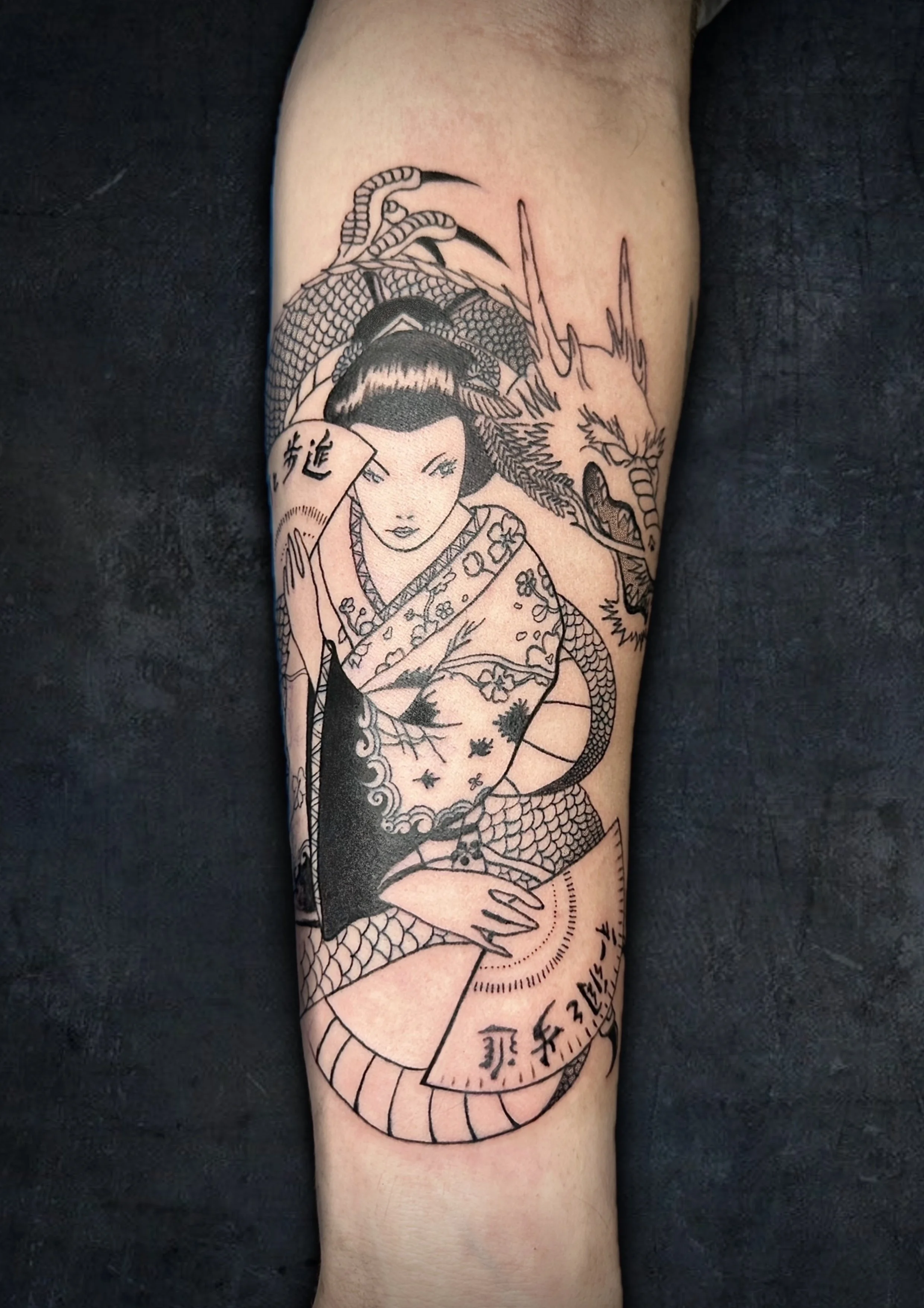 Black and white tattoo featuring a woman with traditional Japanese attire and hairstyle, a fierce dragon, and Japanese characters on the arm.