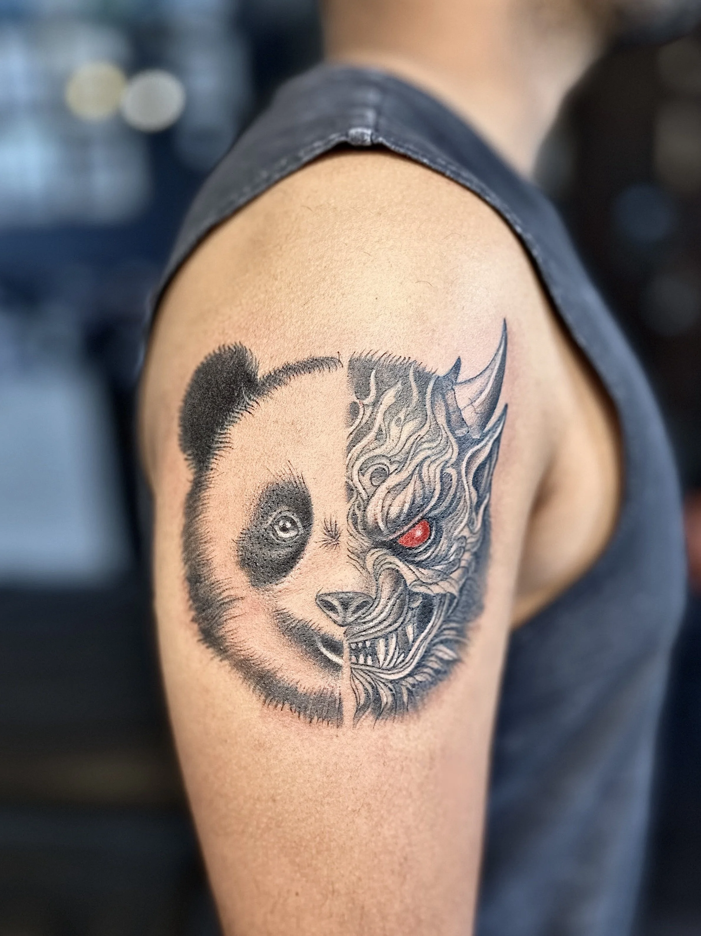 Tattoo on person's upper arm depicting a panda and a demon face, split vertically in the middle.
