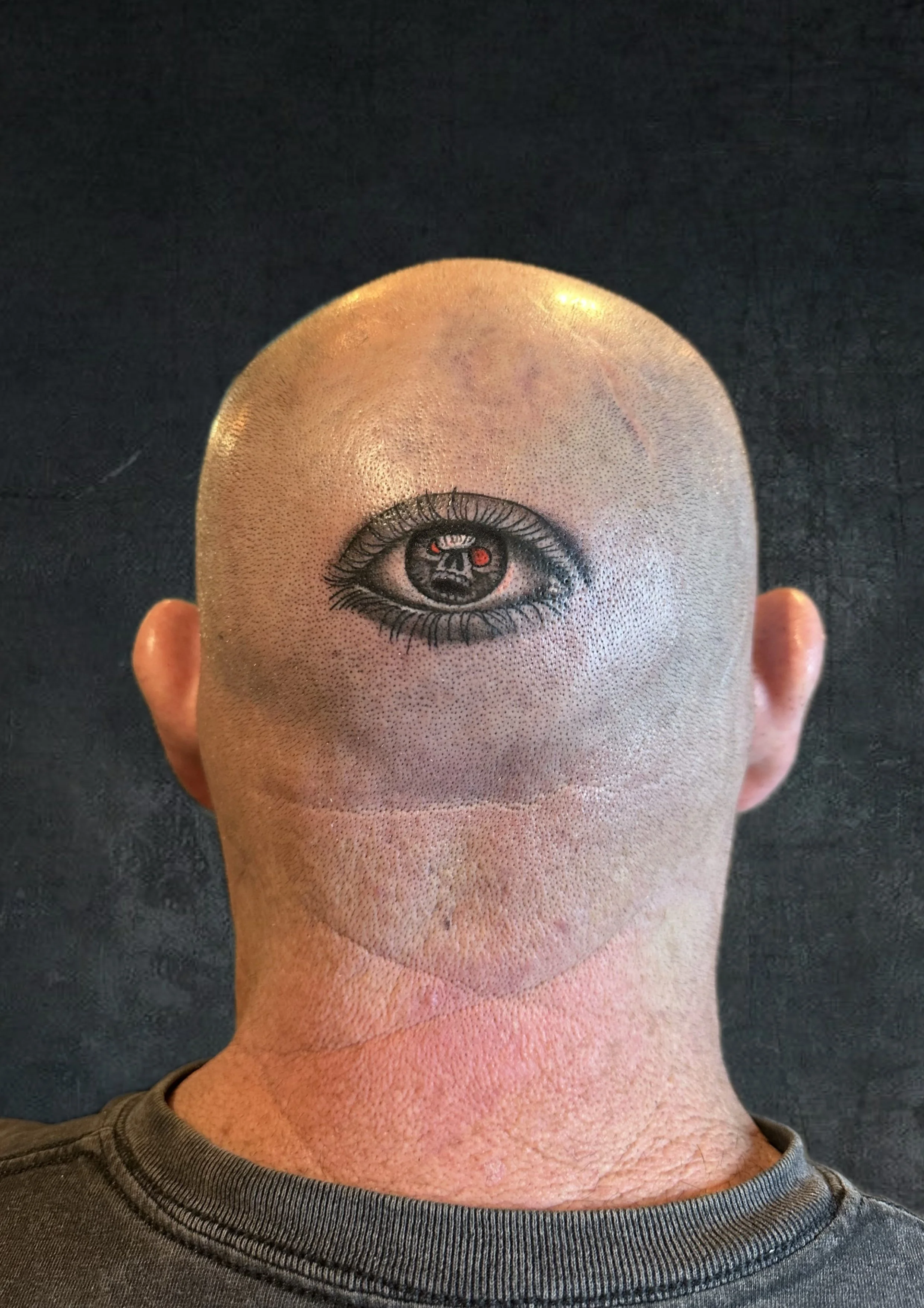 A person with a tattoo of an eye on the back of their bald head.