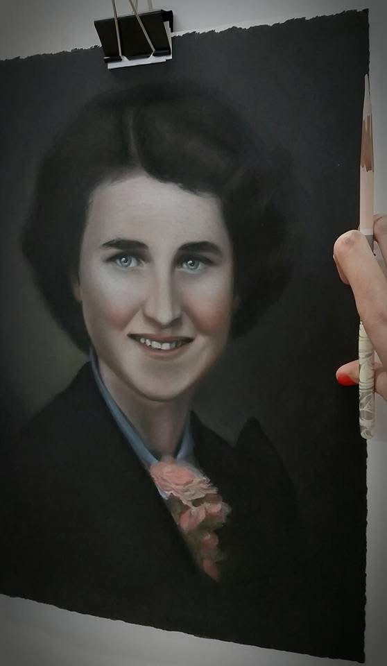 A person is painting a realistic portrait of a woman with blue eyes, dark hair, and a black outfit on a dark canvas. The artist's hand and paintbrush are visible on the right side of the image.