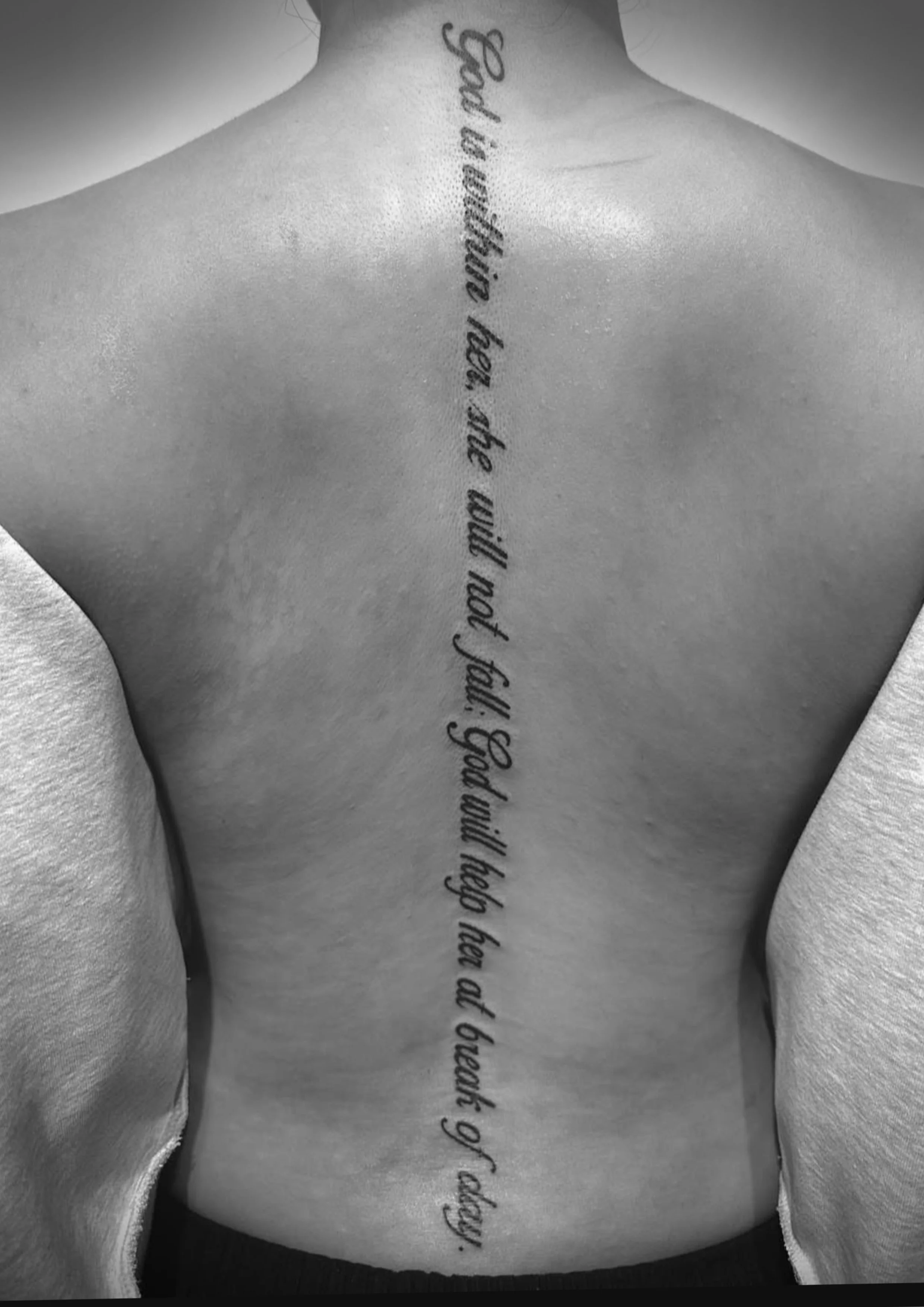 Back of a person's torso with a vertical tattoo of a quote in cursive font.