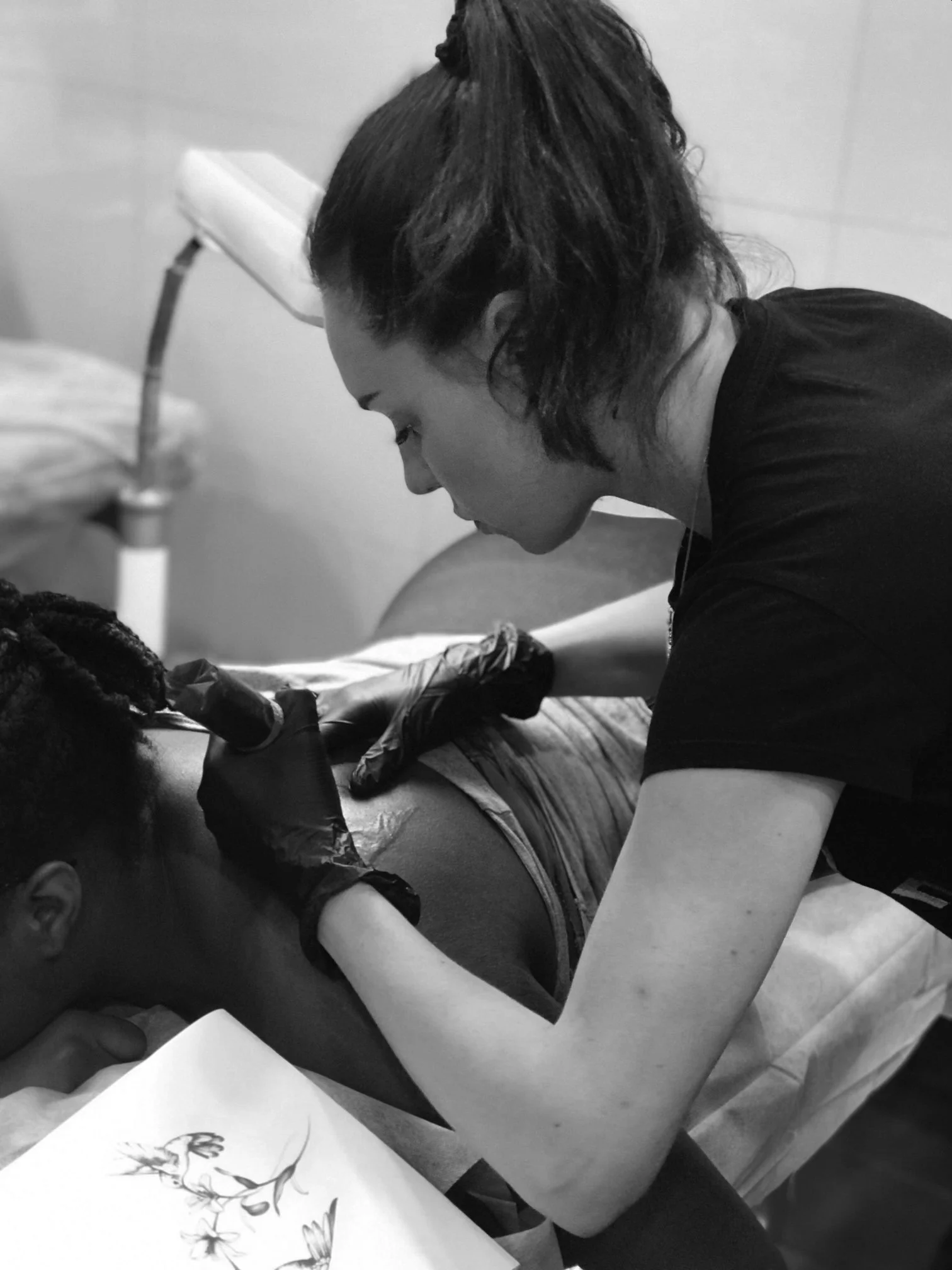 A woman with short dark hair and light skin tattooing a person's arm in a tattoo studio.