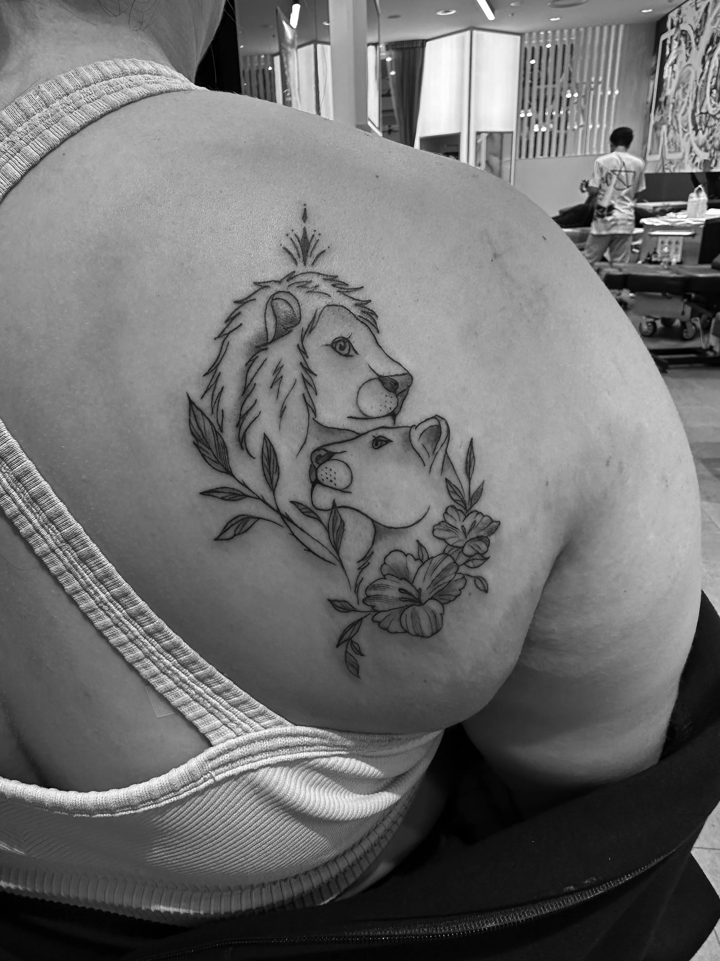 A tattoo of a lion and lioness surrounded by leaves and flowers on a person's upper chest.