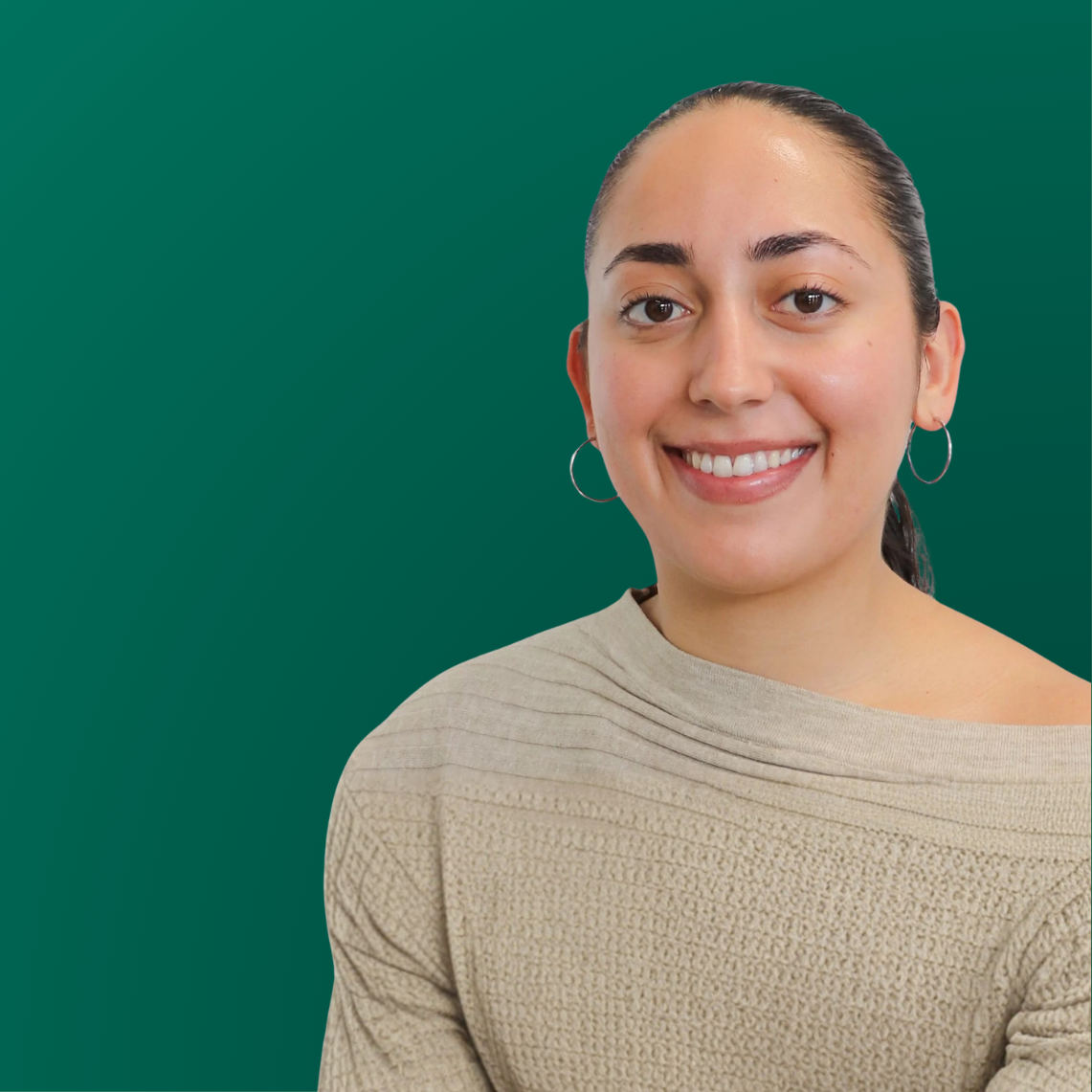 Smiling woman with dark hair tied back, wearing hoop earrings and a beige textured sweater, standing against a green background.