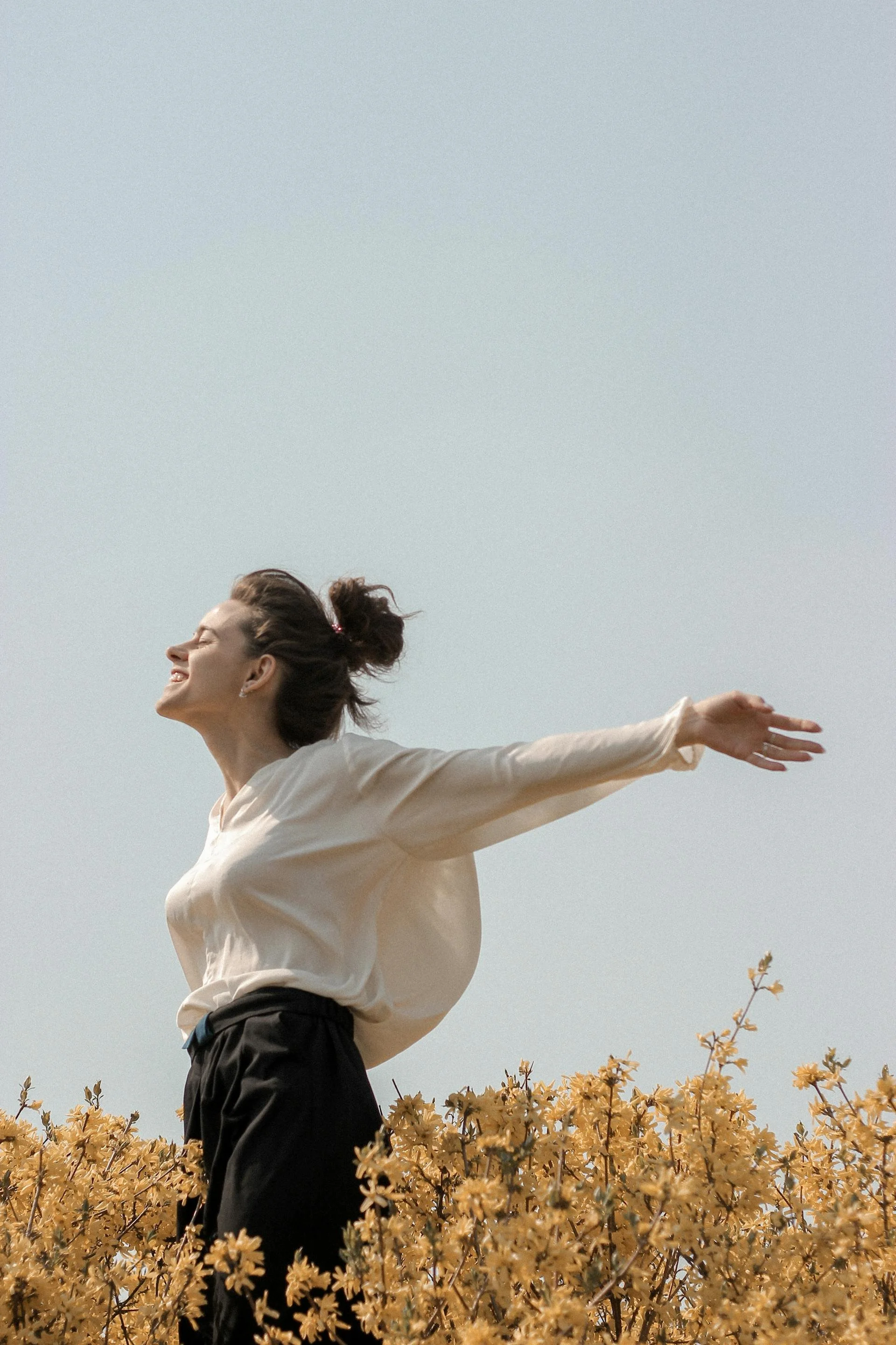 A woman standing in a flower field with her arms outstretched and a joyful expression on her face.