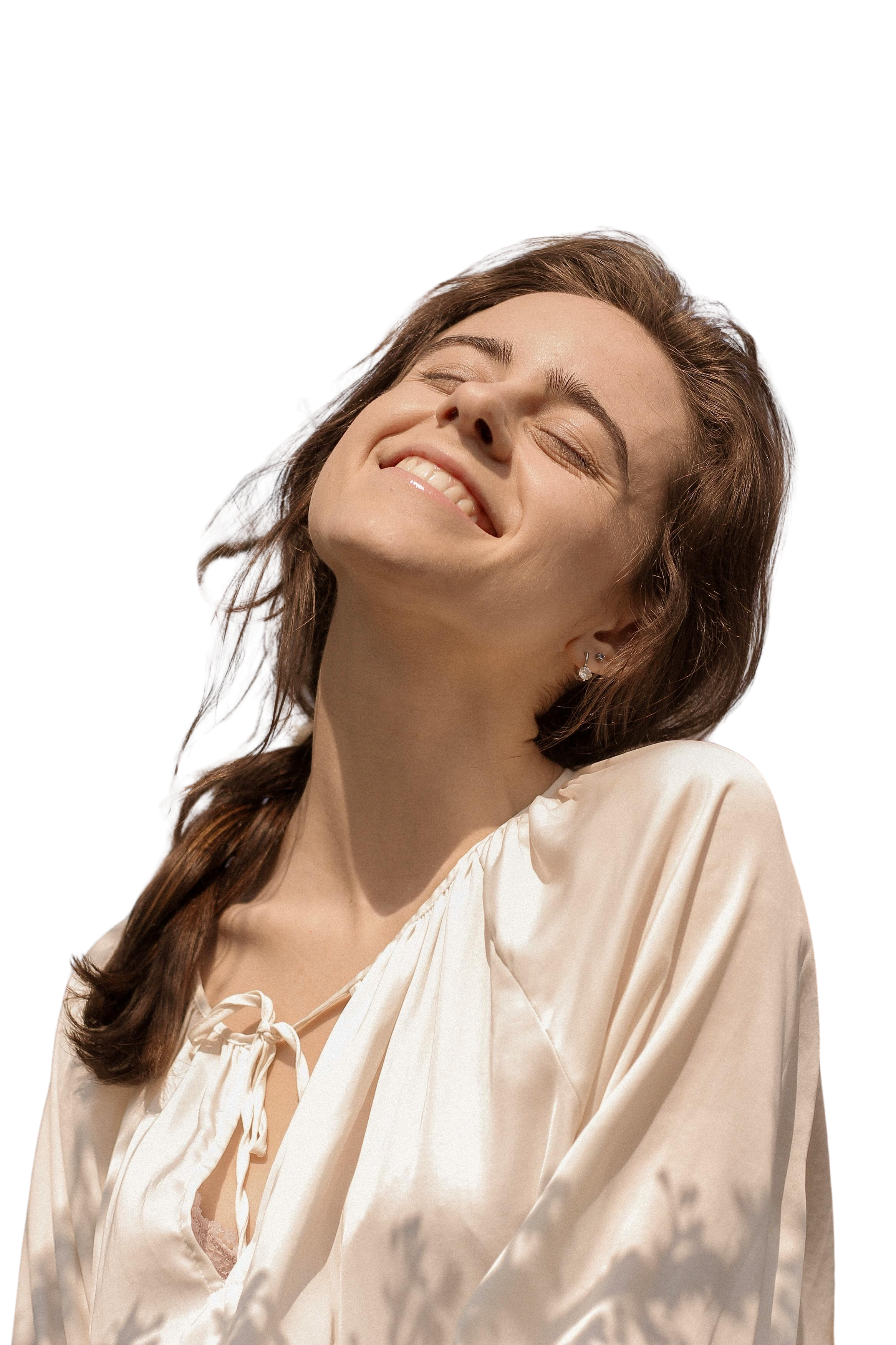 A smiling woman with closed eyes, wearing a light-colored satin blouse and pearl earrings.