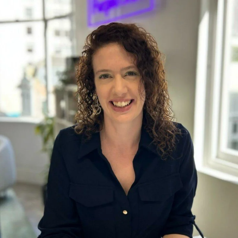 Ruth Hendry smiling, wearing a blue dress, in an office