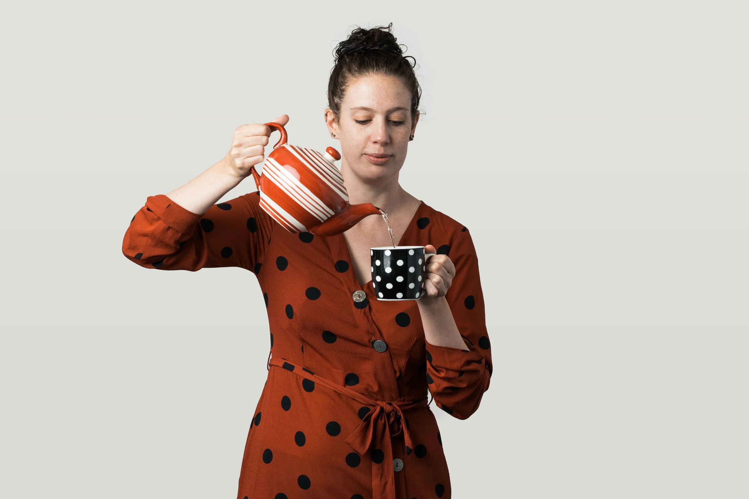 Ruth Hendry pouring tea from a striped tea pot into a spotted mug, wearing a spotted dress.