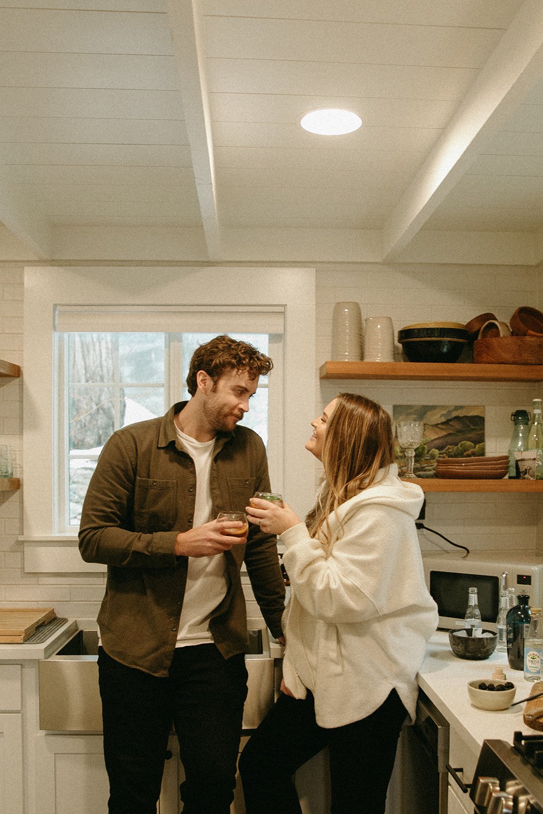 Engaged couple standing in an Airbnb kitchen toasting with cocktails