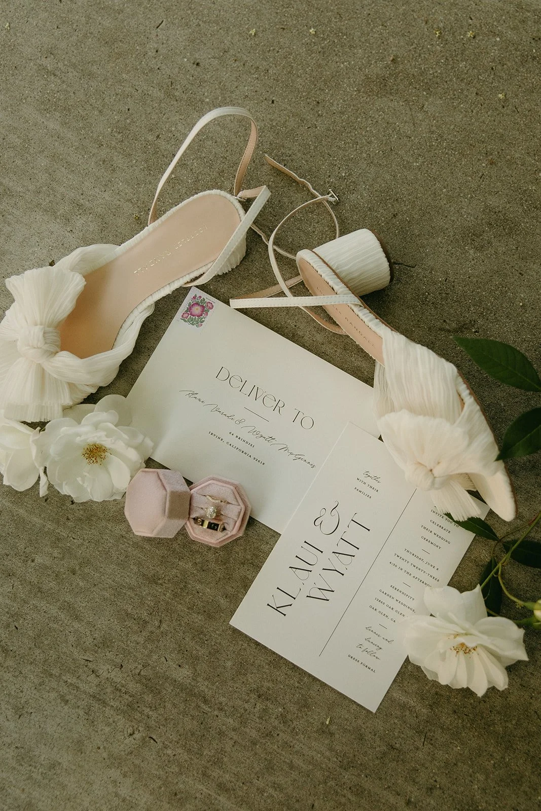 A flat-lay shot of the bride's delicate heels, wedding invitations, and engagement ring, styled perfectly on the ground at Serendipity Garden Weddings.