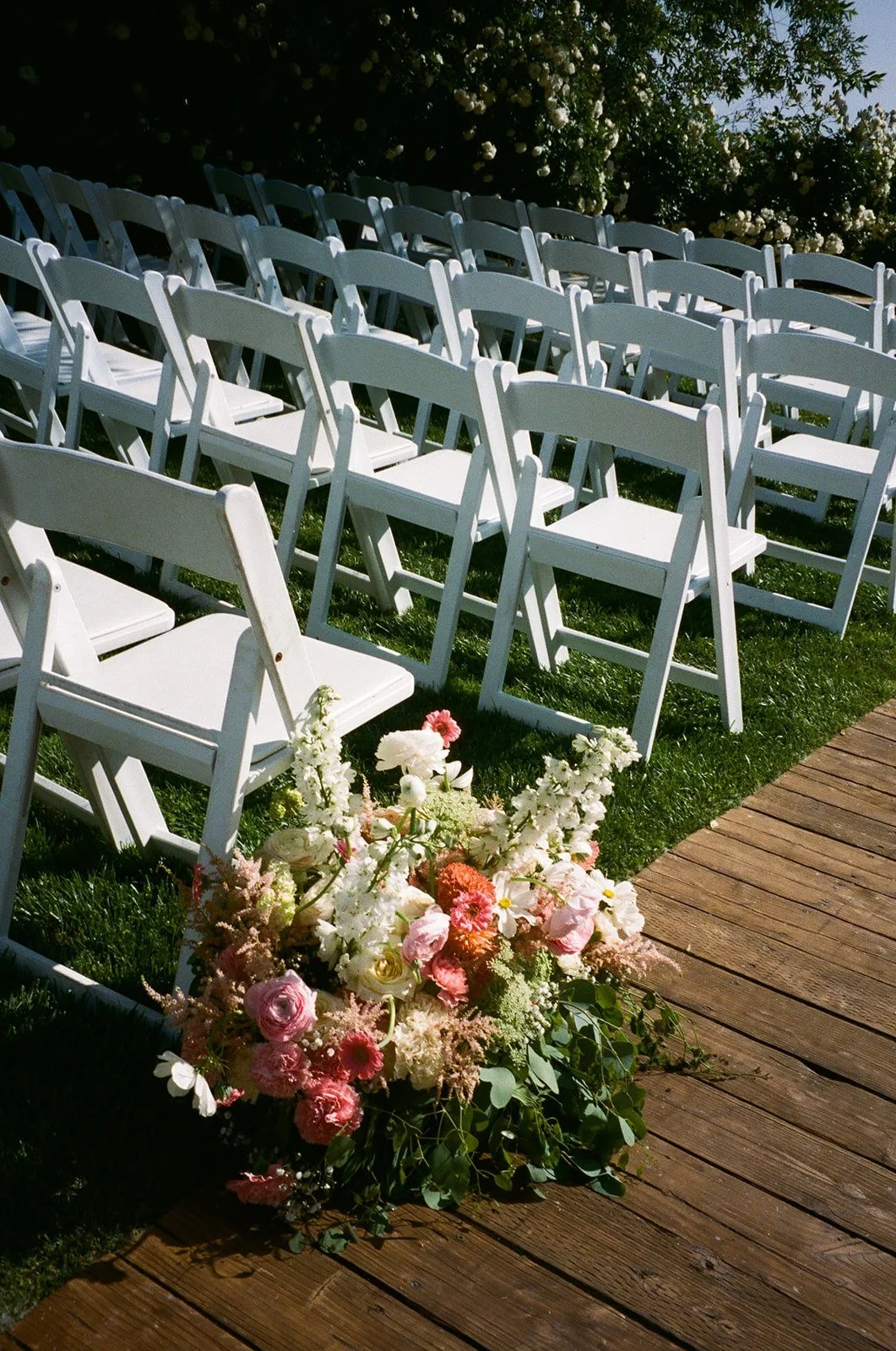 Film photo of A serene view of white chairs arranged for an outdoor wedding ceremony, with vibrant floral arrangements on the lawn.