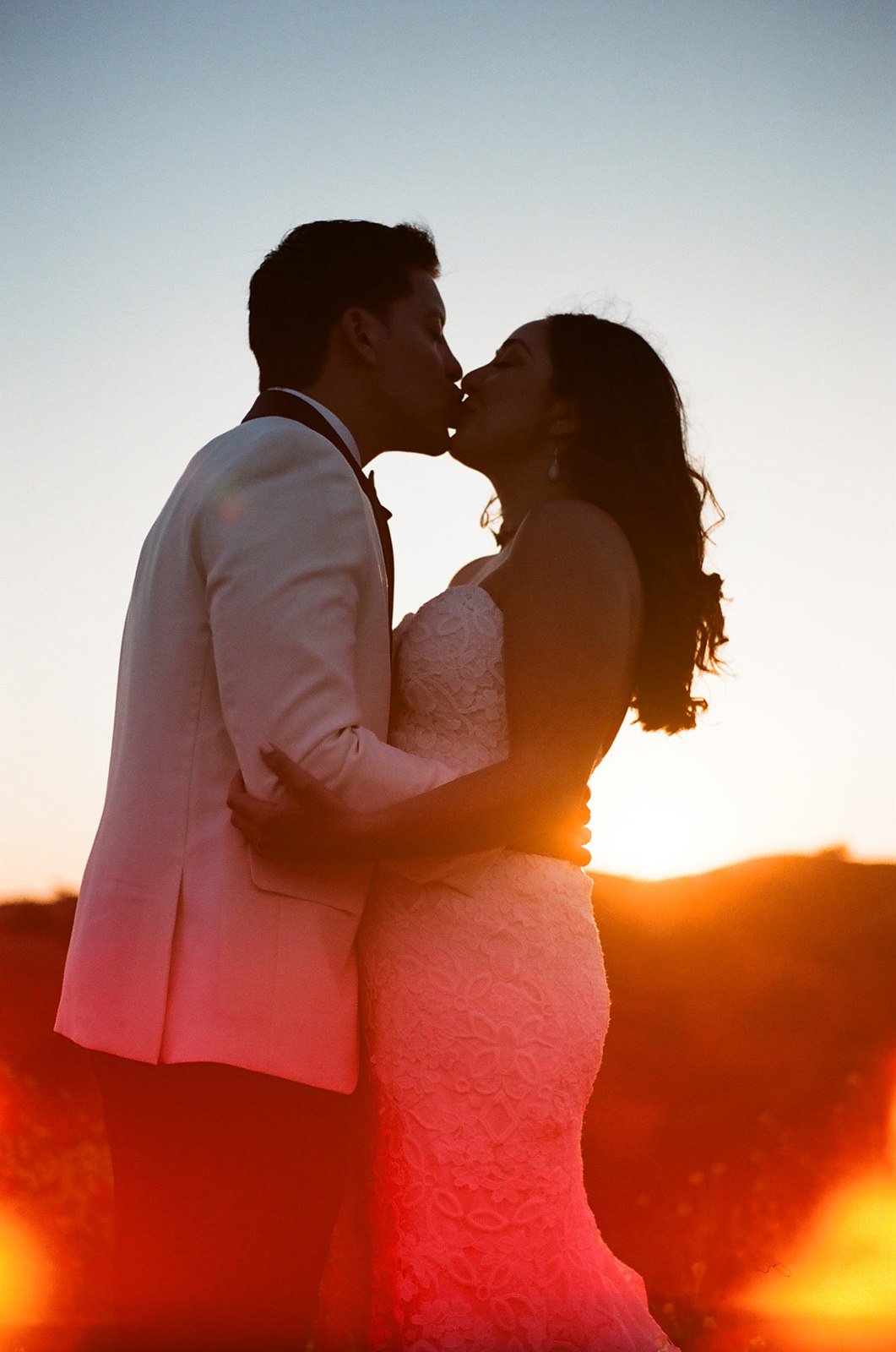 Film wedding photo of bride and groom kissing during sunset