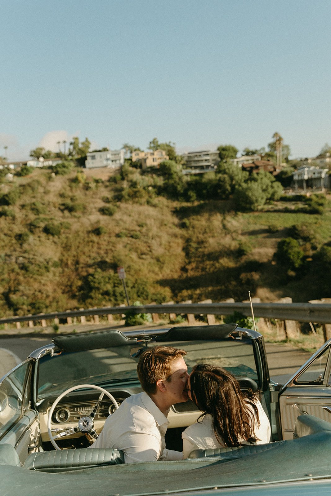 Fun Engagement Photo Ideas - A couple enjoys a ride in a classic convertible along a winding road, capturing the essence of their relationship with a unique engagement photo idea.