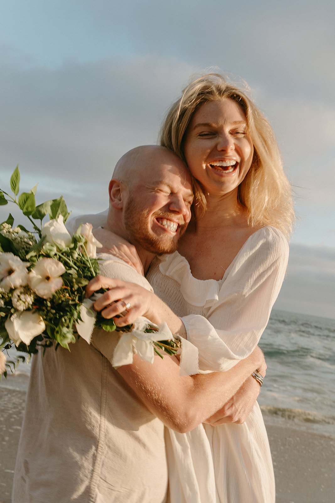 A couple embraces tightly with the ocean breeze in their hair, beaming with joy—capturing candid expressions is a great engagement photo tip.